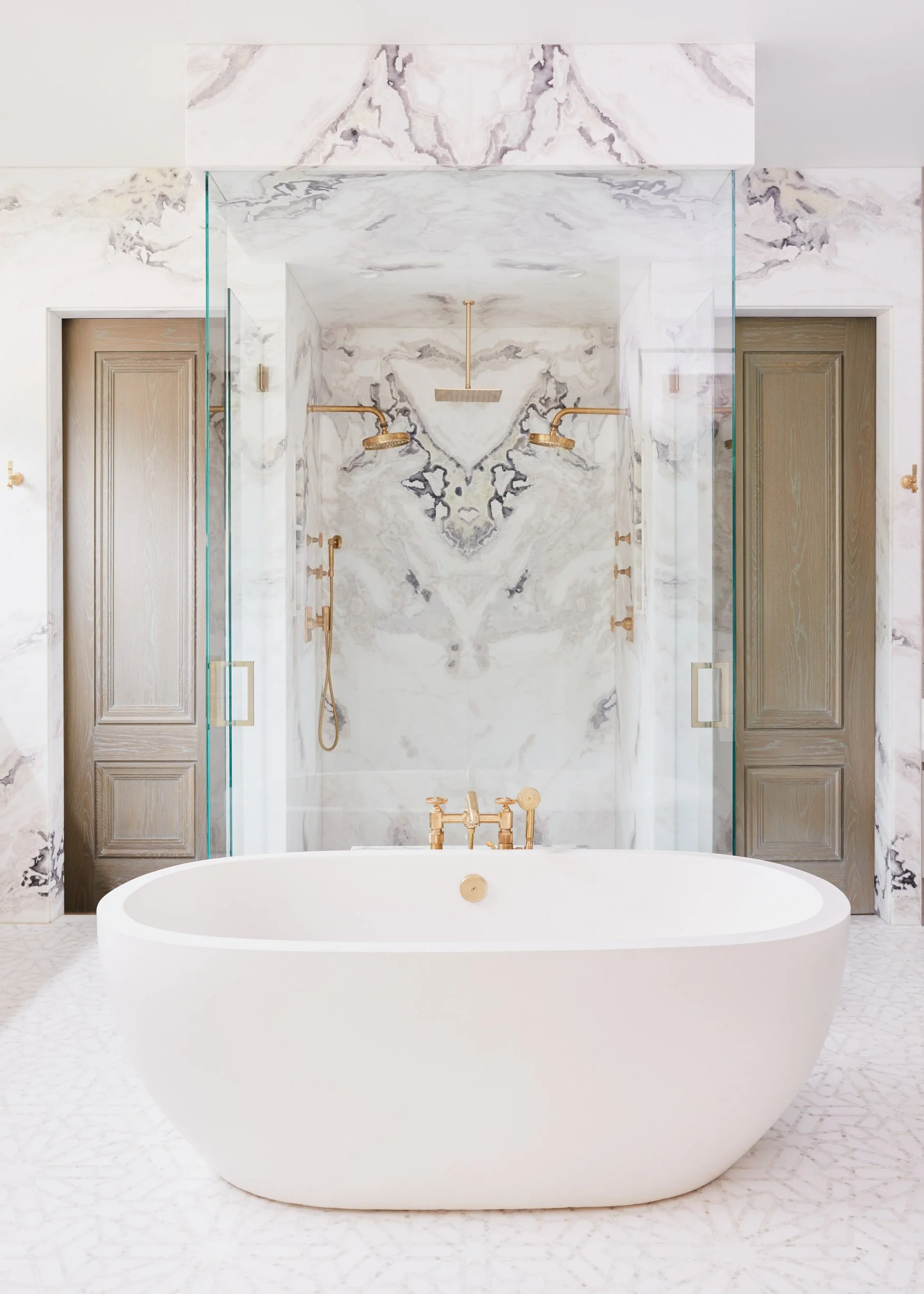  Bookmatched marble shower wall with brass accents and white bathtub.  