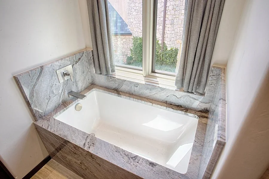  Custom bathtub installation under a window with grey curtains.  