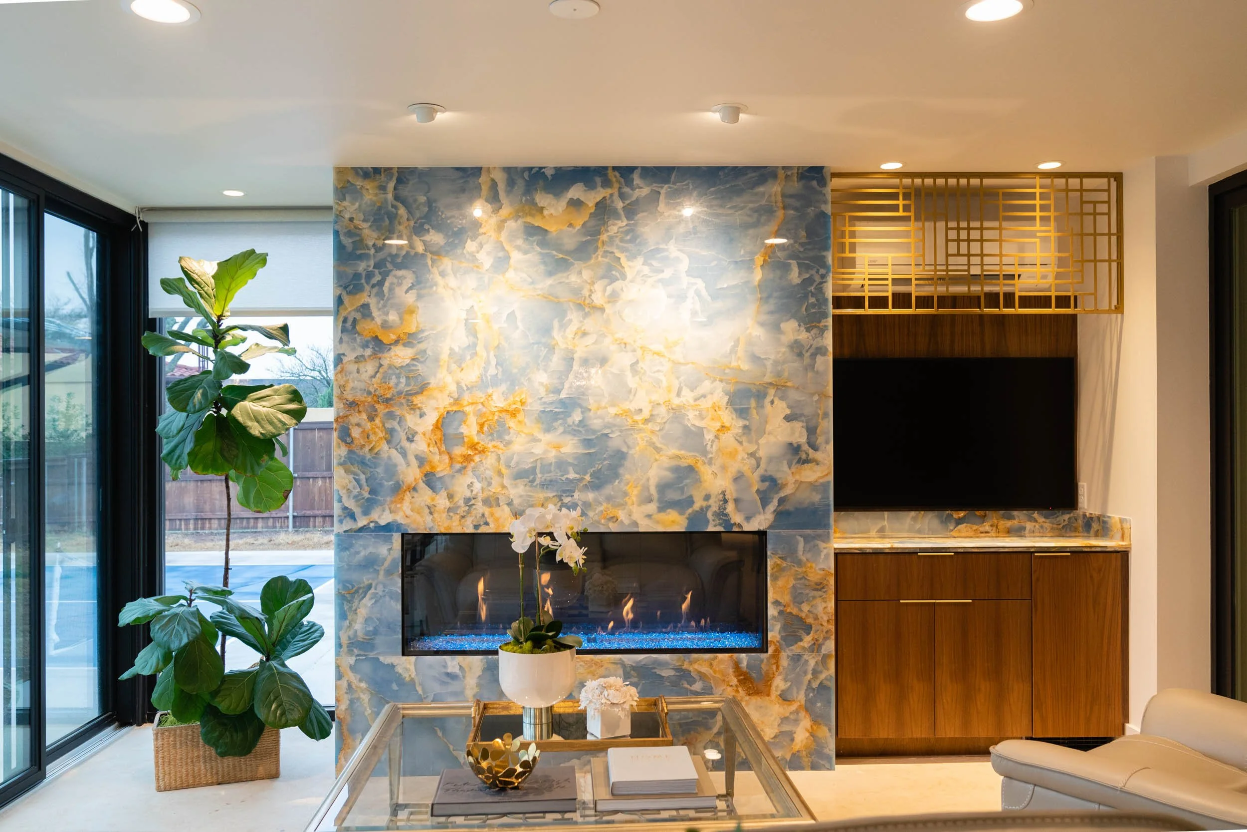  Custom blue onyx fireplace installation with brass accents. Large green plant on the side. 