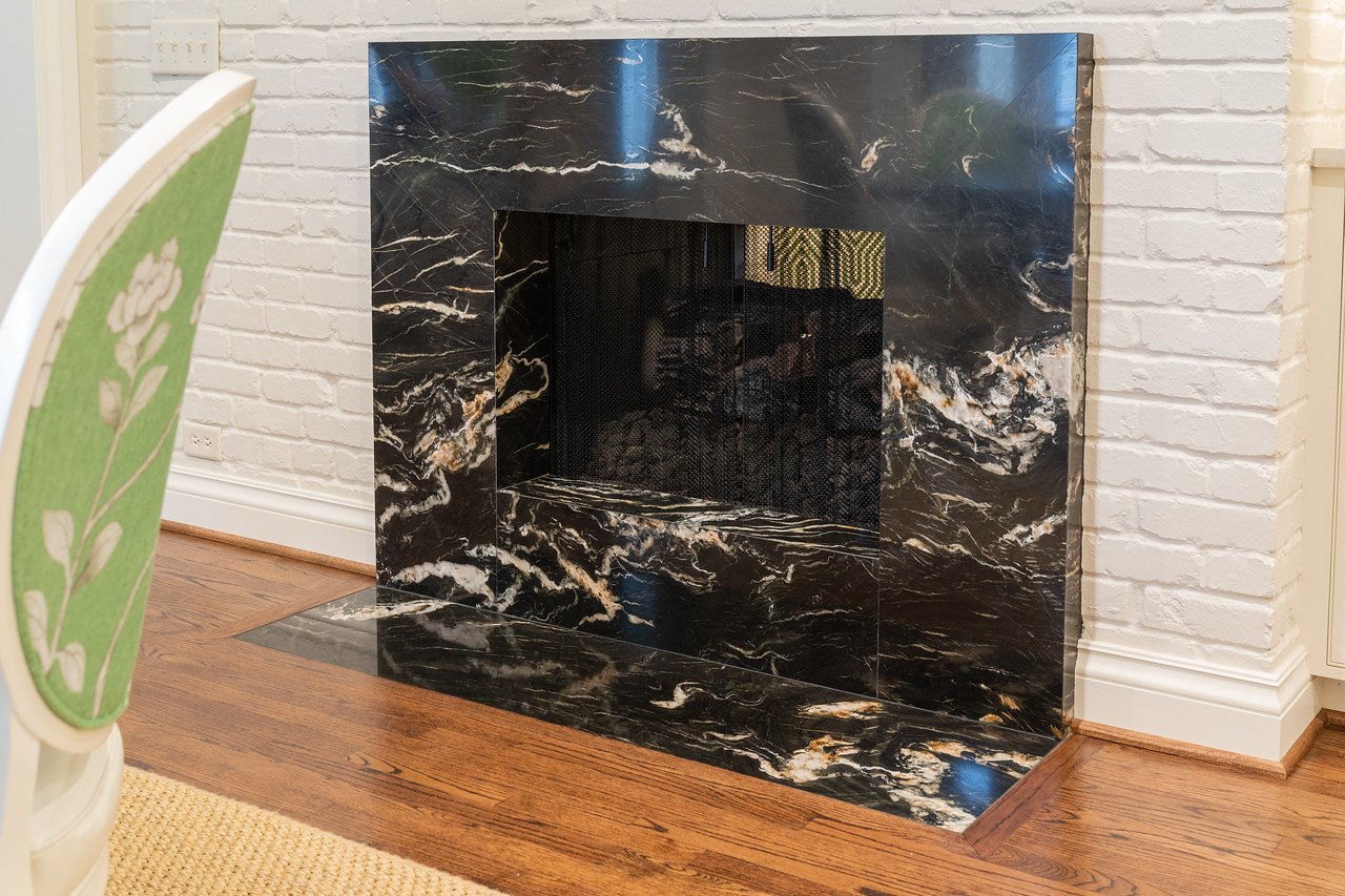  Marble fireplace installation with a white brick wall and wood floors. 