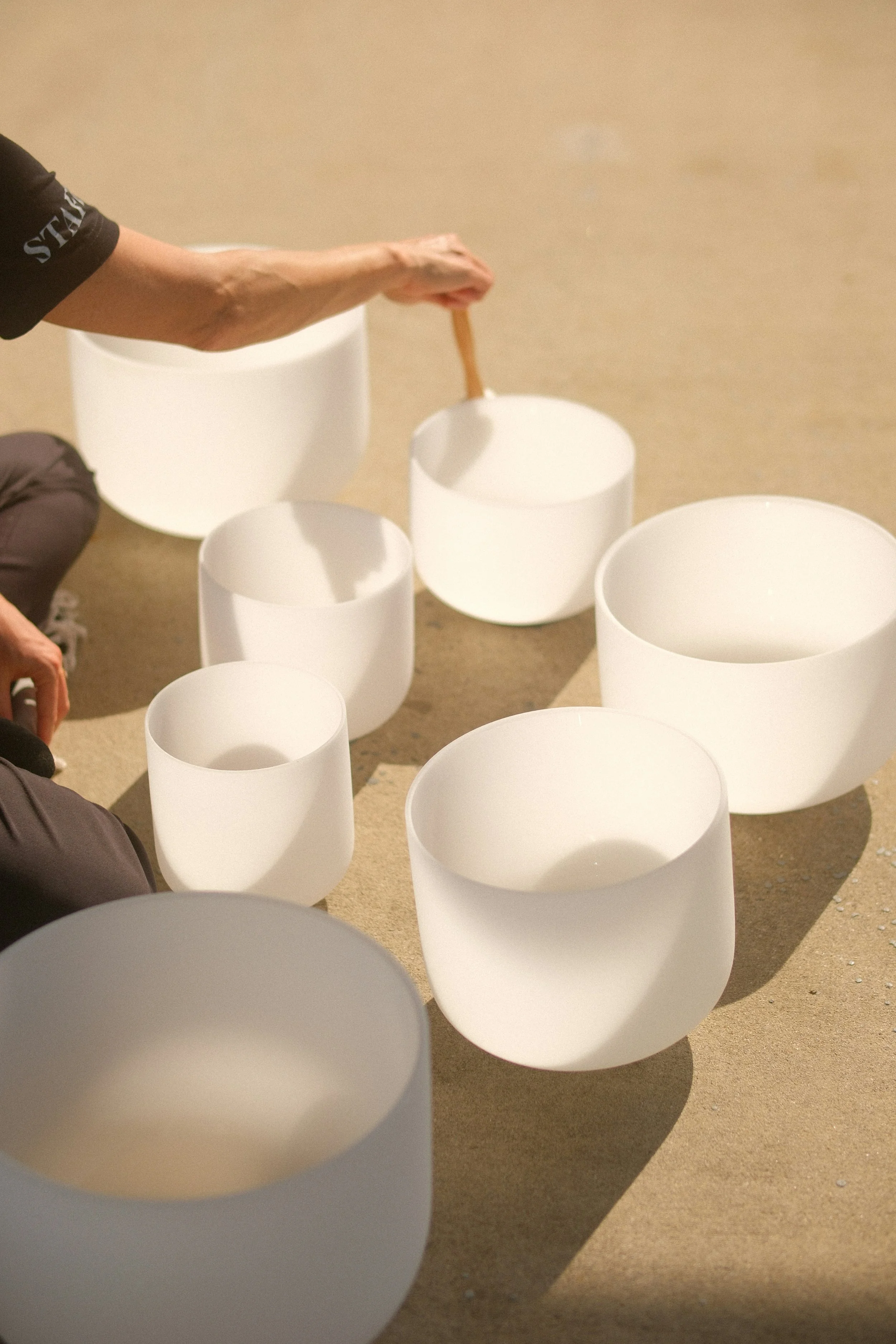 Person playing white crystal singing bowls on the floor in a circle.