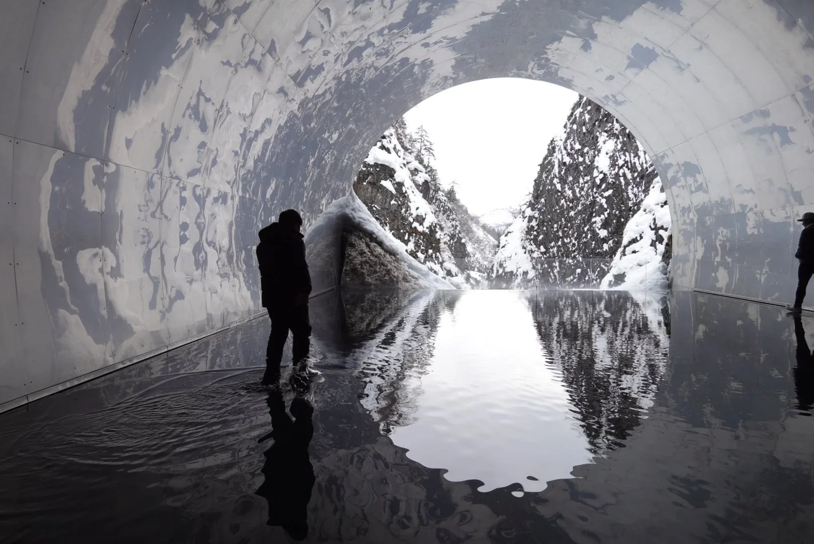 Art museum of Tokamachi Niigata in the winter with a pool of water in front of the end of a tunnel. The pool of water reflects the stillness of the nature around it.