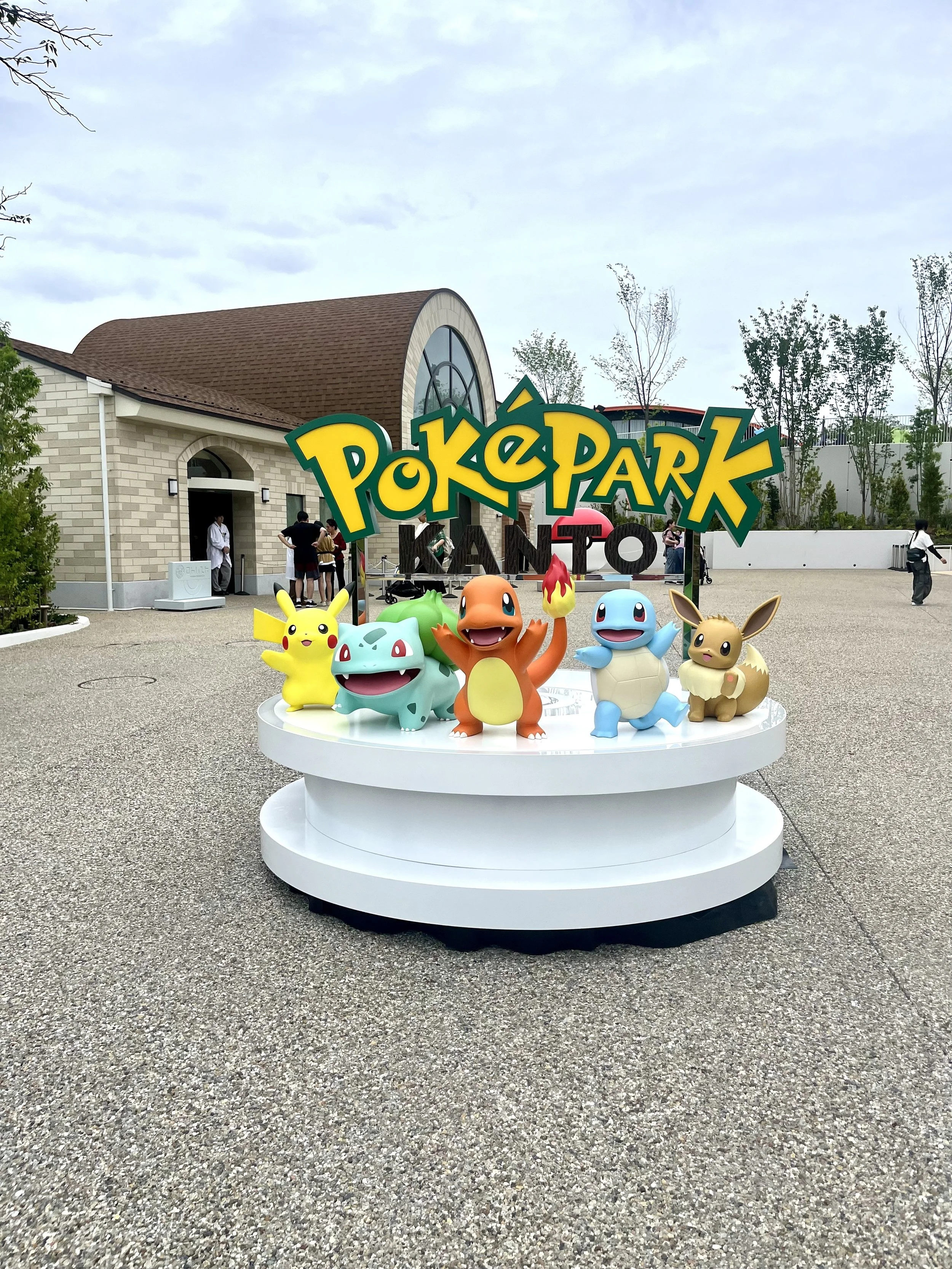 PokéPark KANTO entrance at Yomiuriland in Tokyo featuring statues of Pikachu, Charmander, Squirtle, Bulbasaur, and Eevee beneath the park's colorful sign. The themed entrance welcomes visitors to the Pokémon attraction.