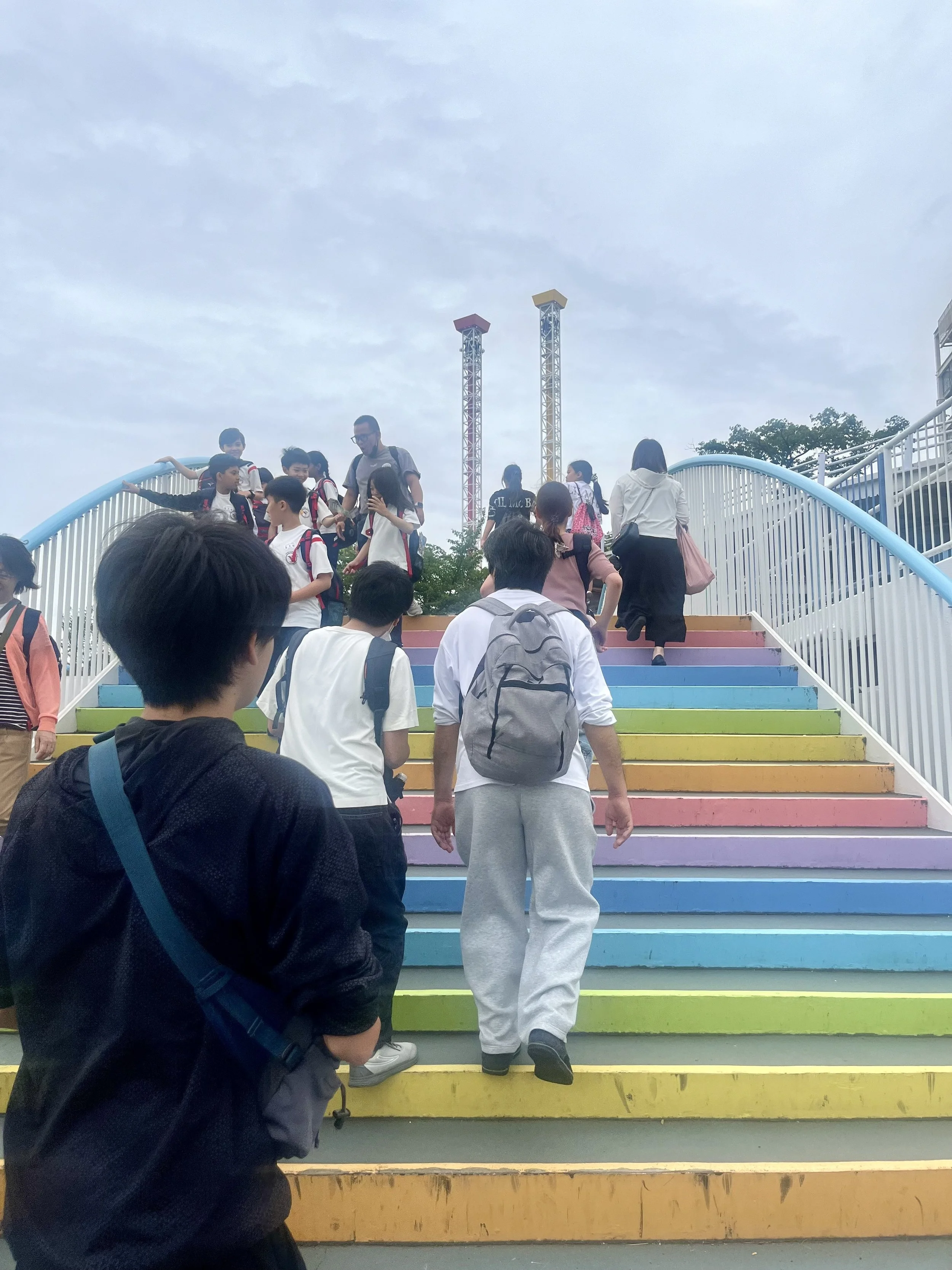 Visitors walking up Yomiuriland's colorful Rainbow Stairs in Tokyo on their way to the amusement park attractions. The vibrant staircase is a popular entrance feature and photo spot for guests.