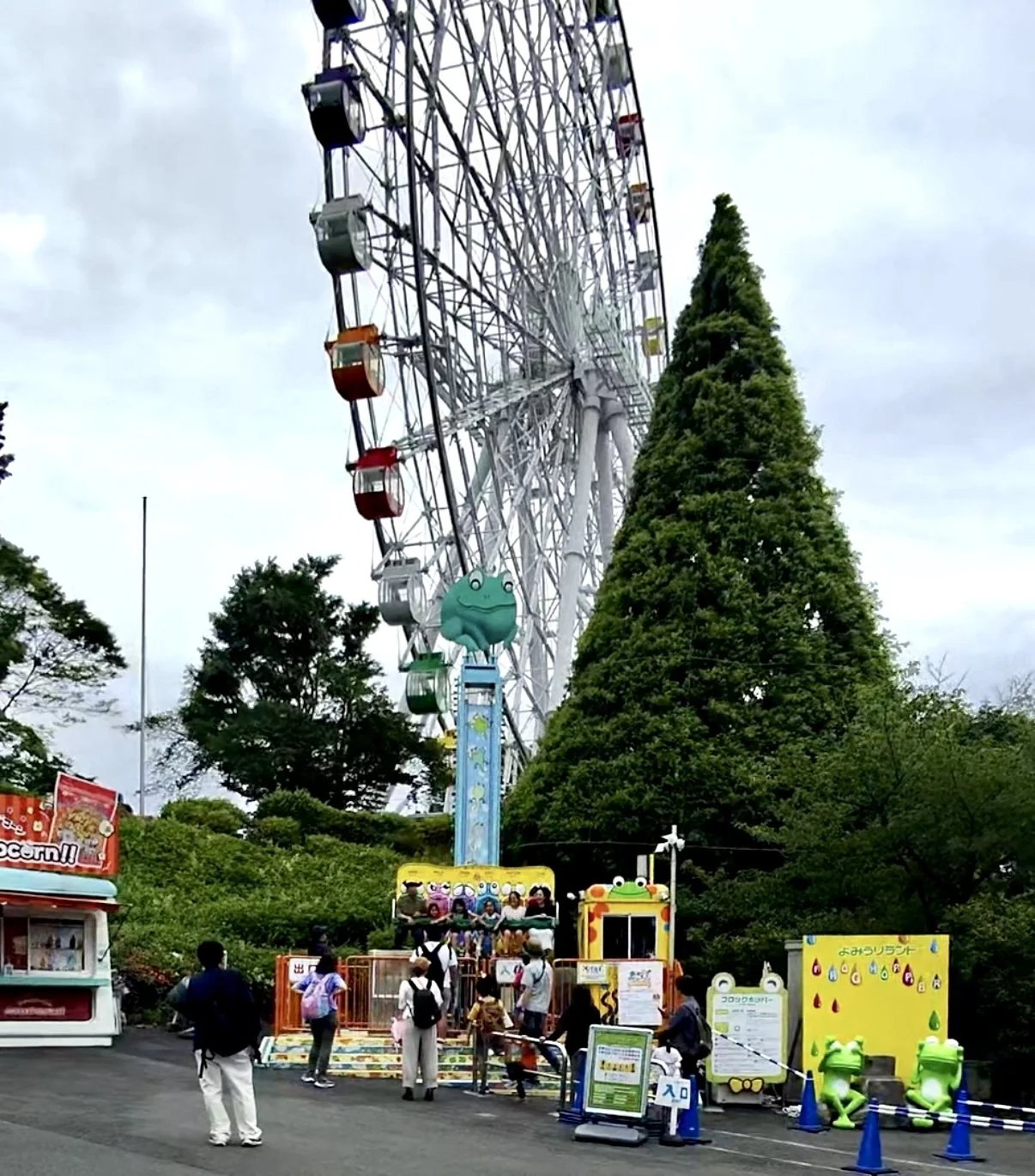 Large Ferris wheel towering over attractions at Yomiuriland amusement park in Tokyo. Visitors walk through the park while enjoying rides and family friendly entertainment.