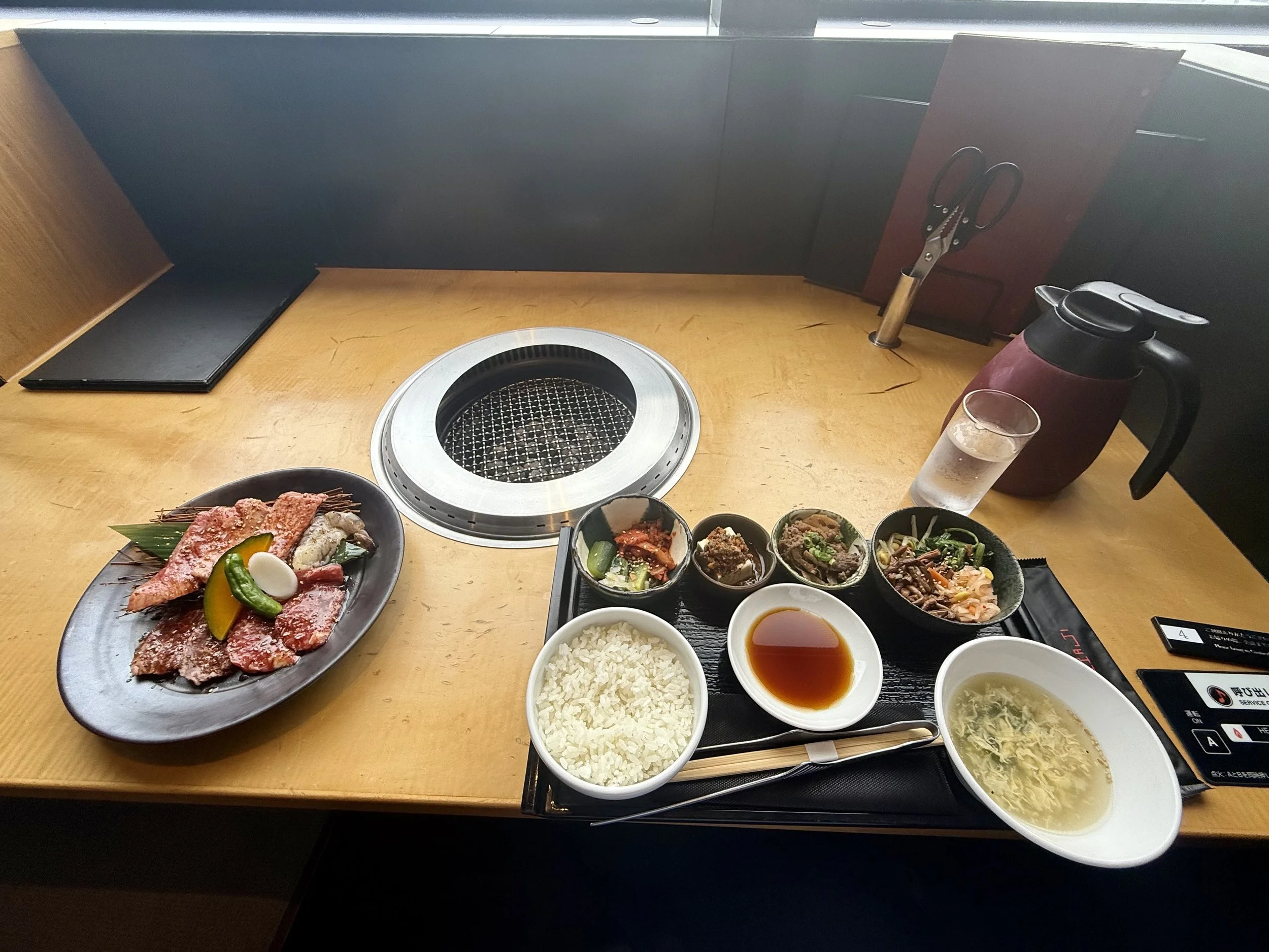 Japanese yakiniku set meal with premium wagyu beef, tabletop charcoal grill, steamed rice, soup, dipping sauce, and assorted side dishes at a restaurant in Tokyo.