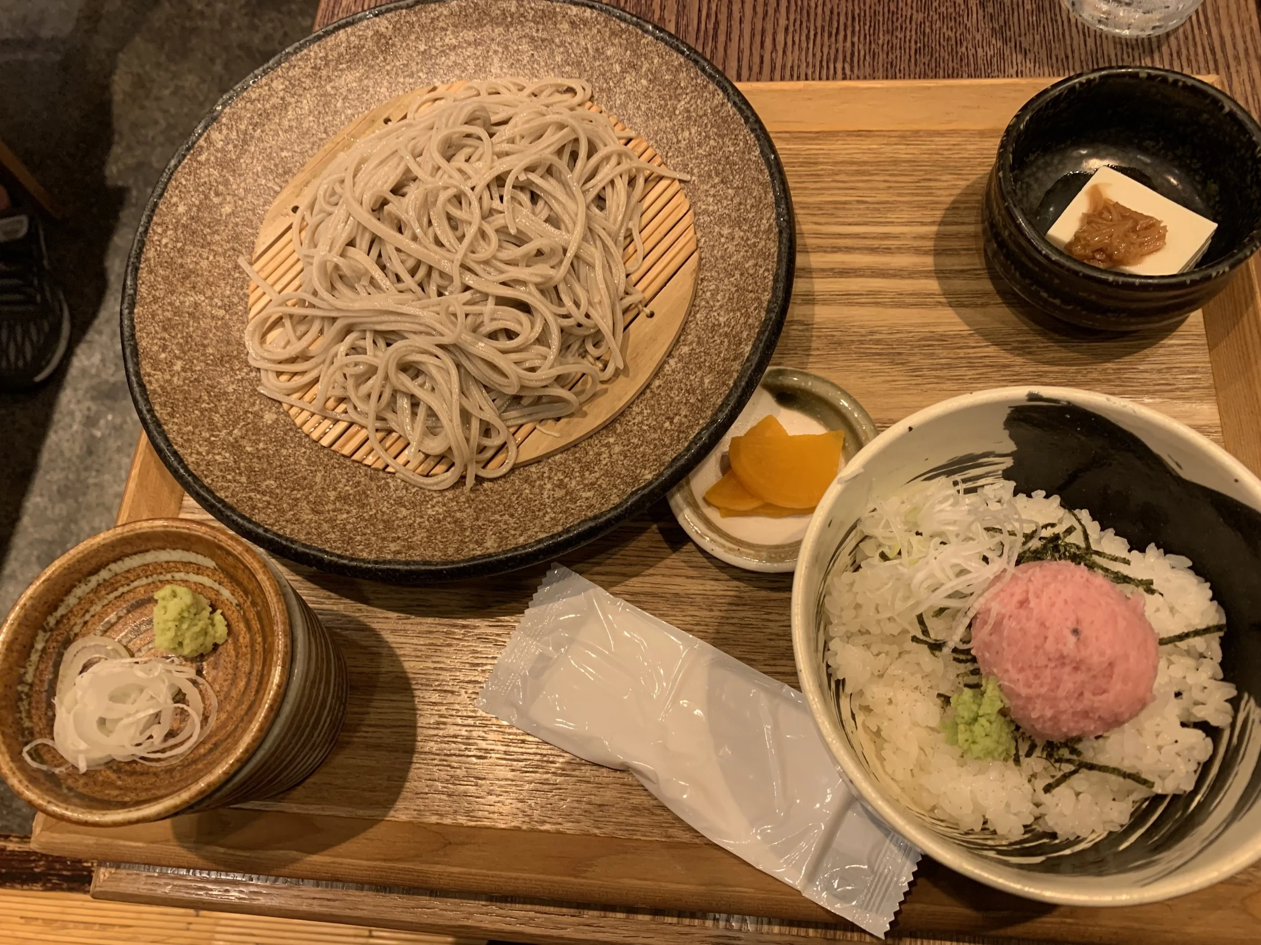 Cold soba noodles served with dipping sauce, wasabi, negi, and a rice bowl topped with minced tuna at a traditional restaurant in Tokyo.