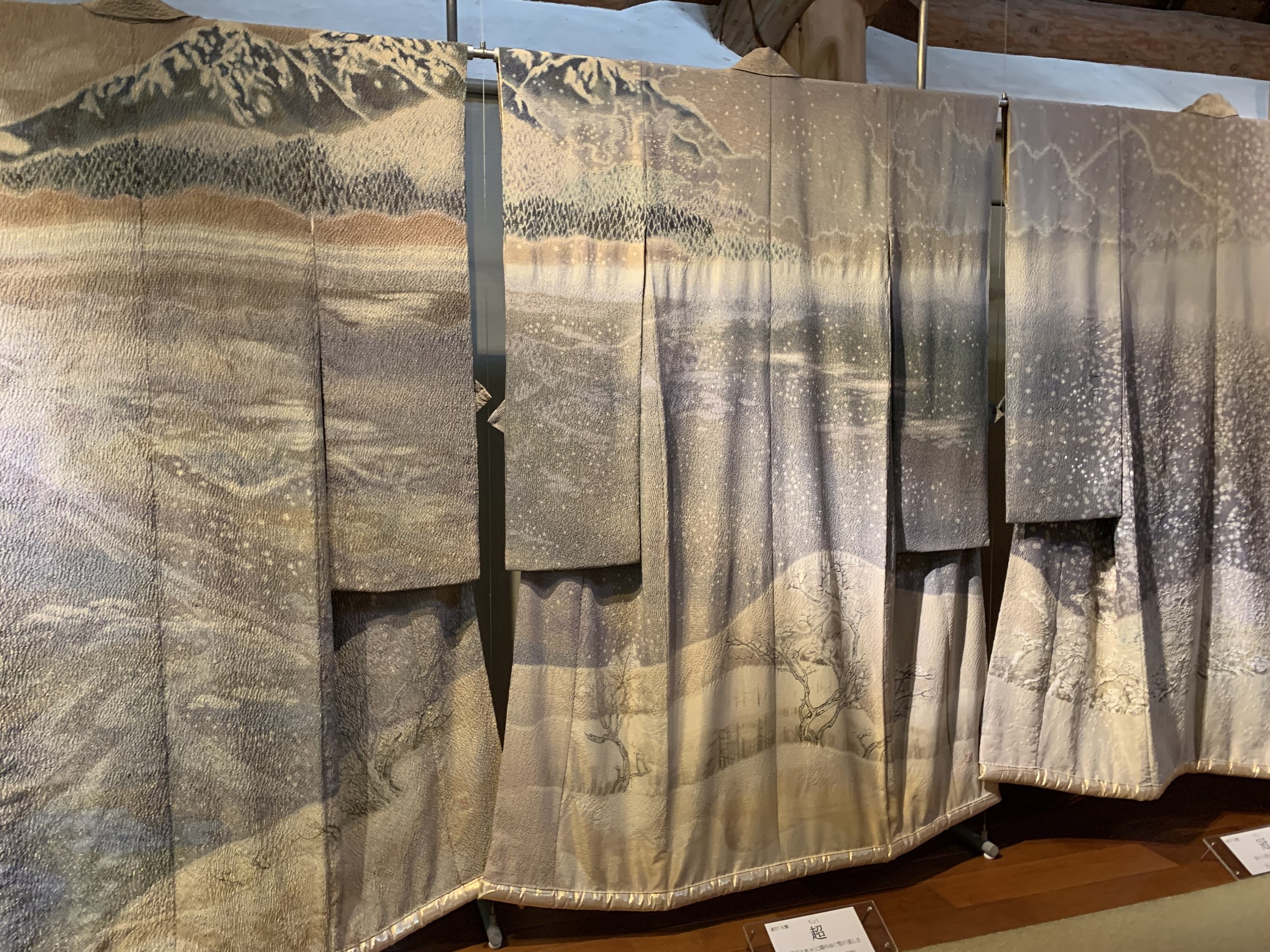 Several hand painted and shibori or tye-dyed pastel-colored kimonos hang on display in a museum near Mount Fuji in Japan.