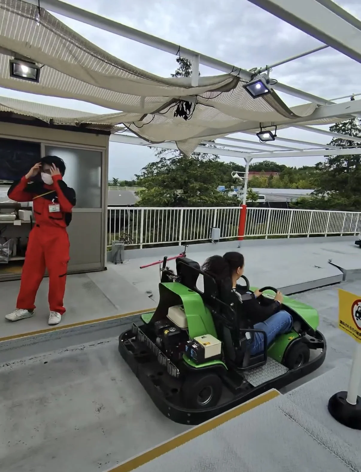 Visitor driving a green go kart at Yomiuriland amusement park in Tokyo while a staff member prepares the attraction for the next riders. The go kart ride is one of the park's family friendly attractions.