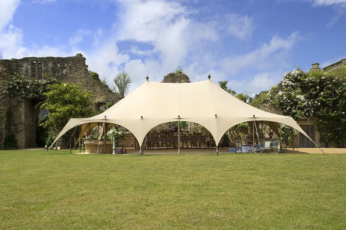 Outdoor event canopy in historic garden setting with stone walls and lush greenery.