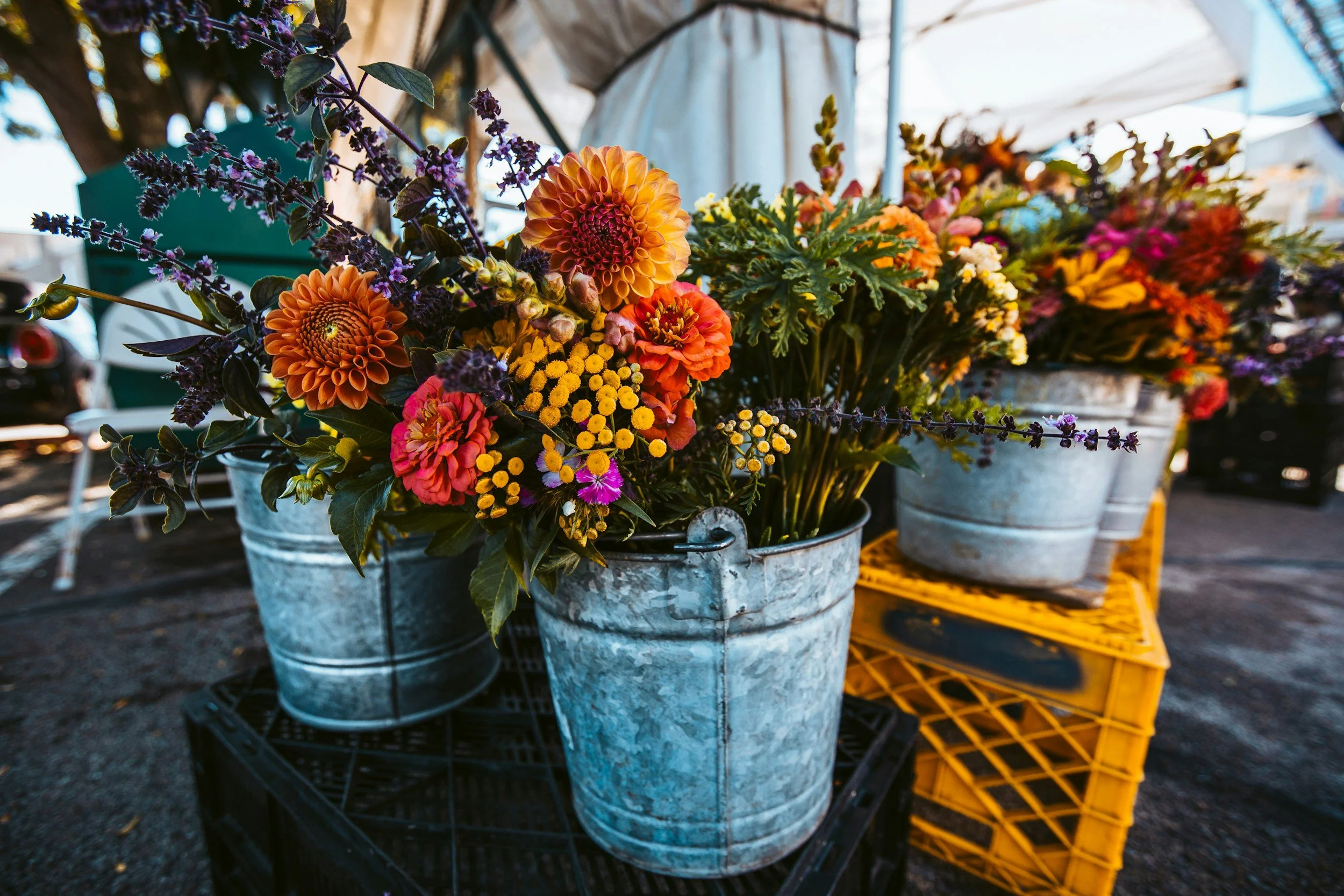 Colorful flower bouquets in weathered metal buckets at an outdoor market.