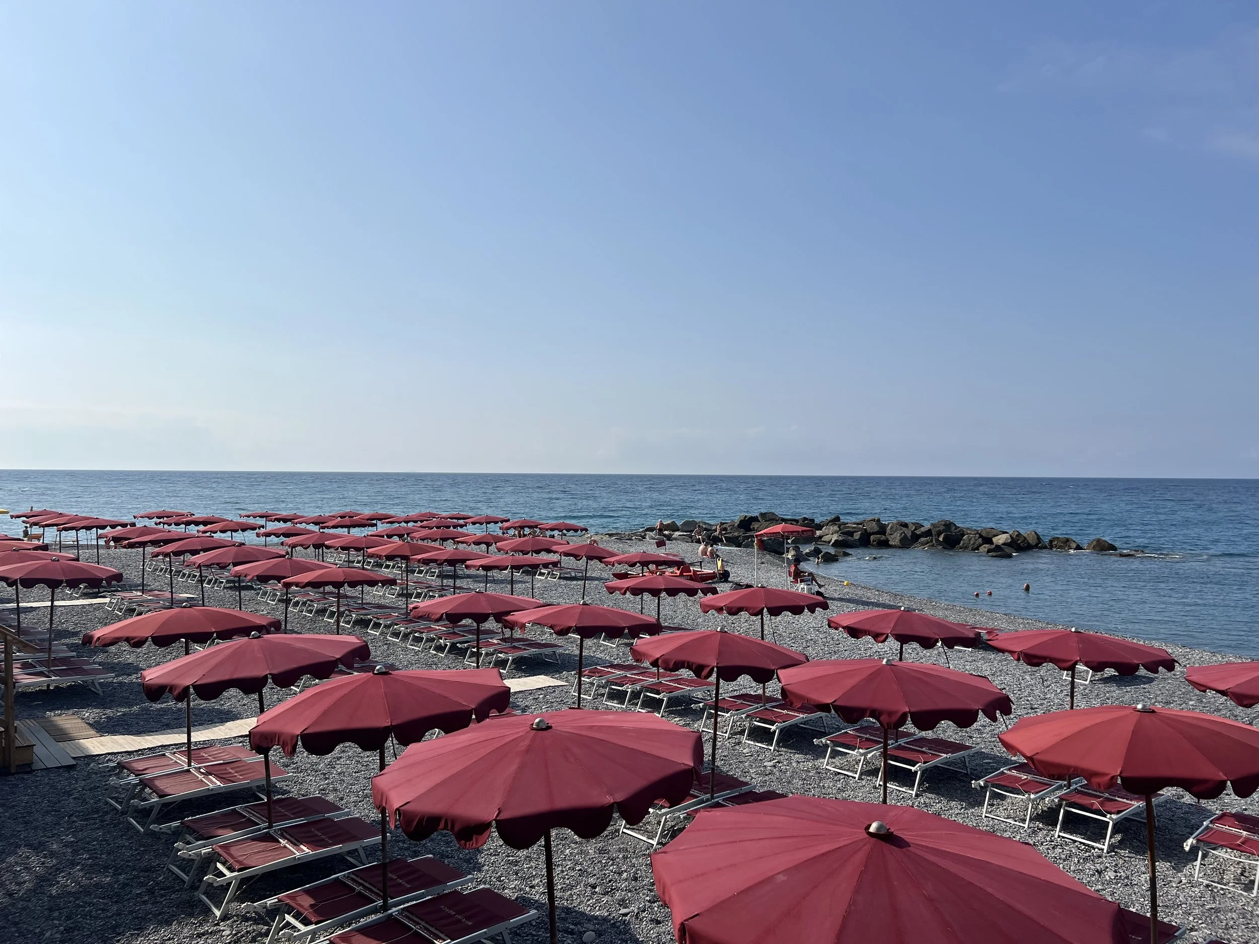 Spiaggia con ombrelloni rossi e sedie sulla spiaggia, vista sul Mar Mediterraneo con cielo sereno a Bordighera.