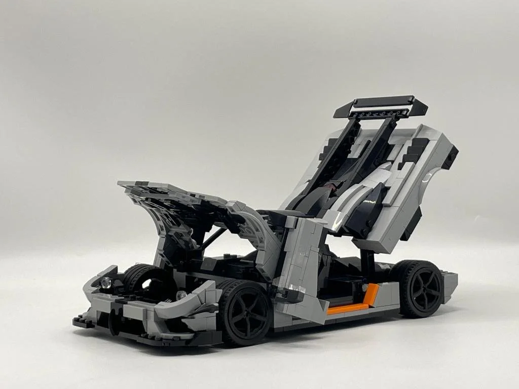 LEGO model of a race car with an open cockpit and raised rear wing, built mostly in gray and black with some orange details.
