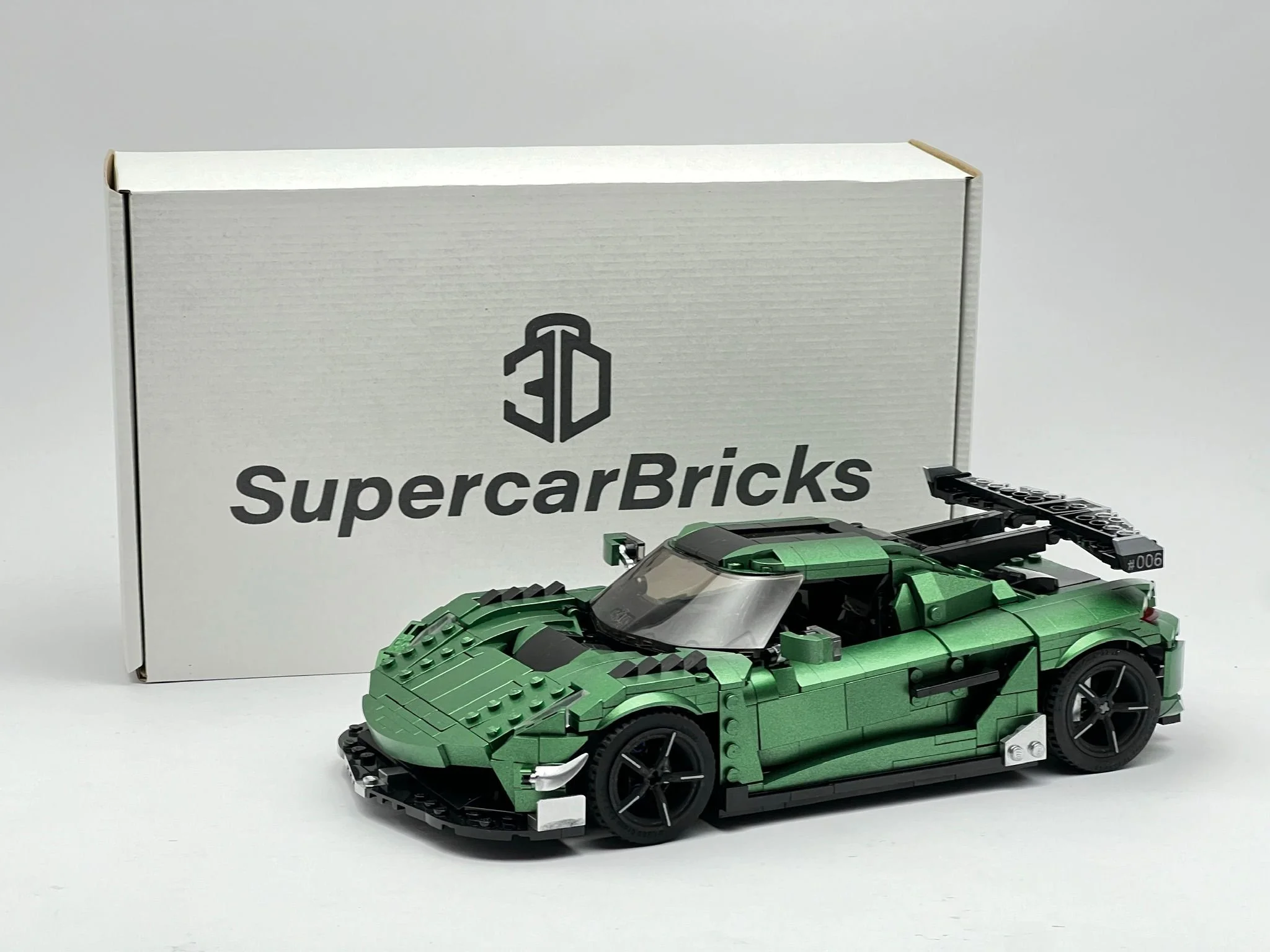Green LEGO model of a race car with a black rear wing, positioned in front of a white 3D Super Car Bricks box with a black logo.