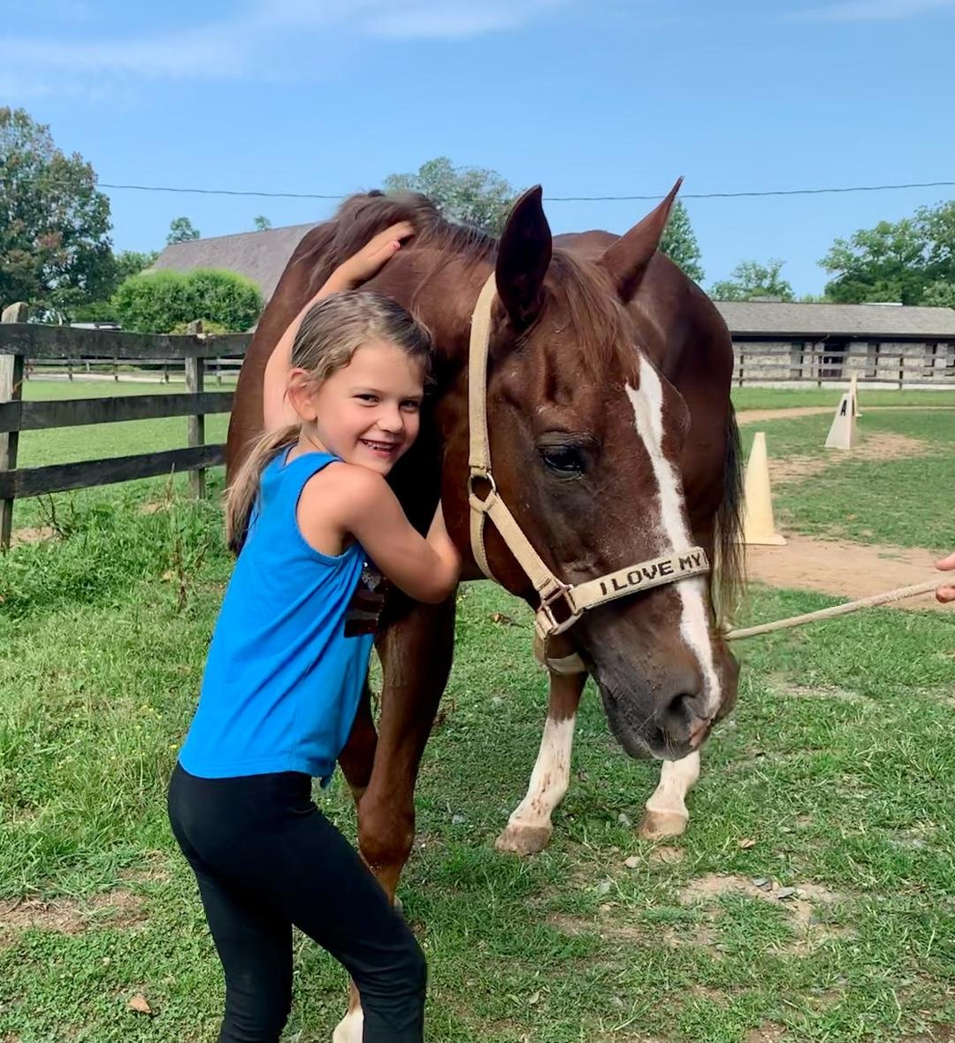 A young girl smiling and hugging a brown horse with a white stripe on its face at a farm.