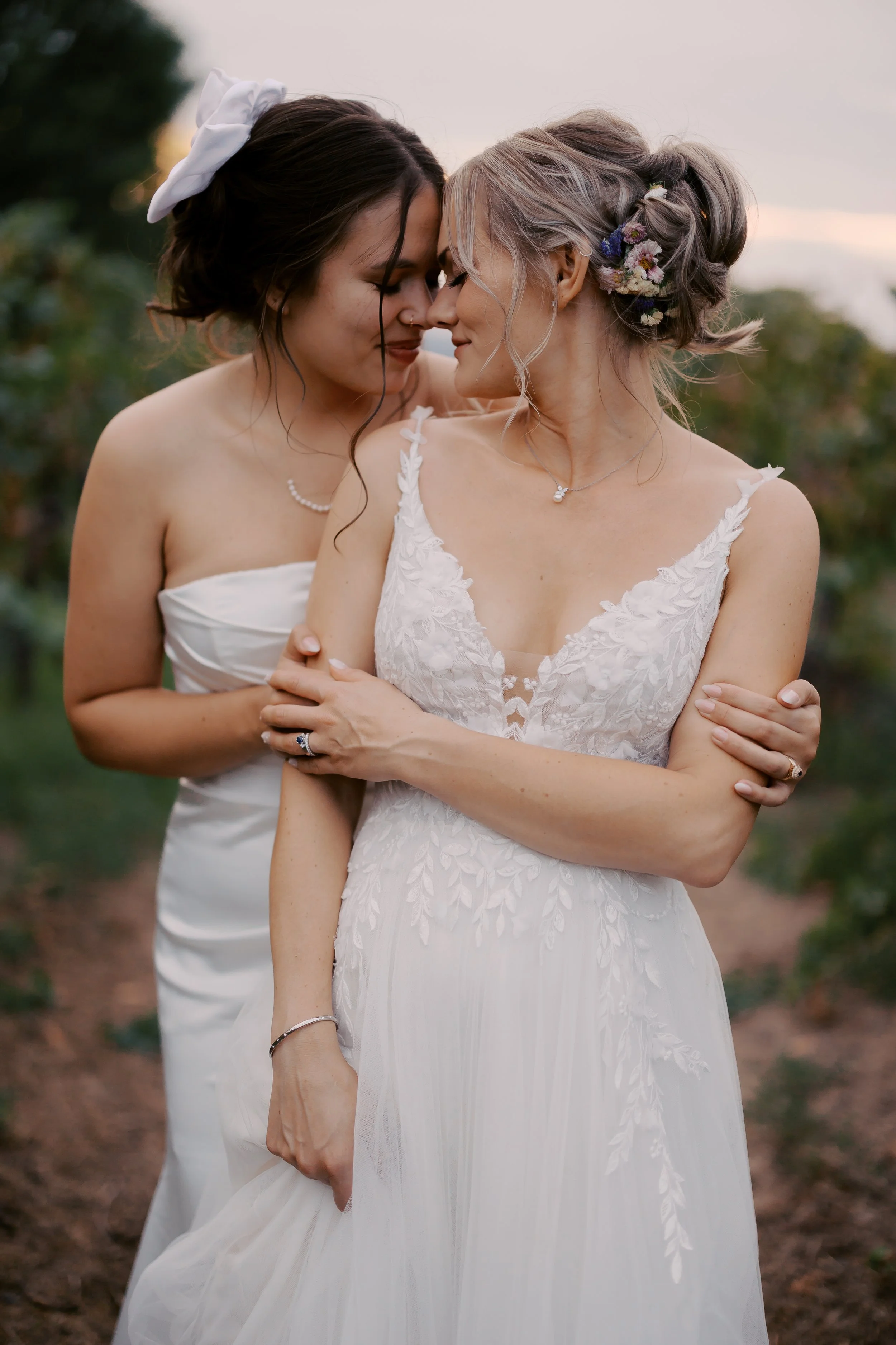 Two women in wedding dresses sharing an intimate moment outdoors during sunset.