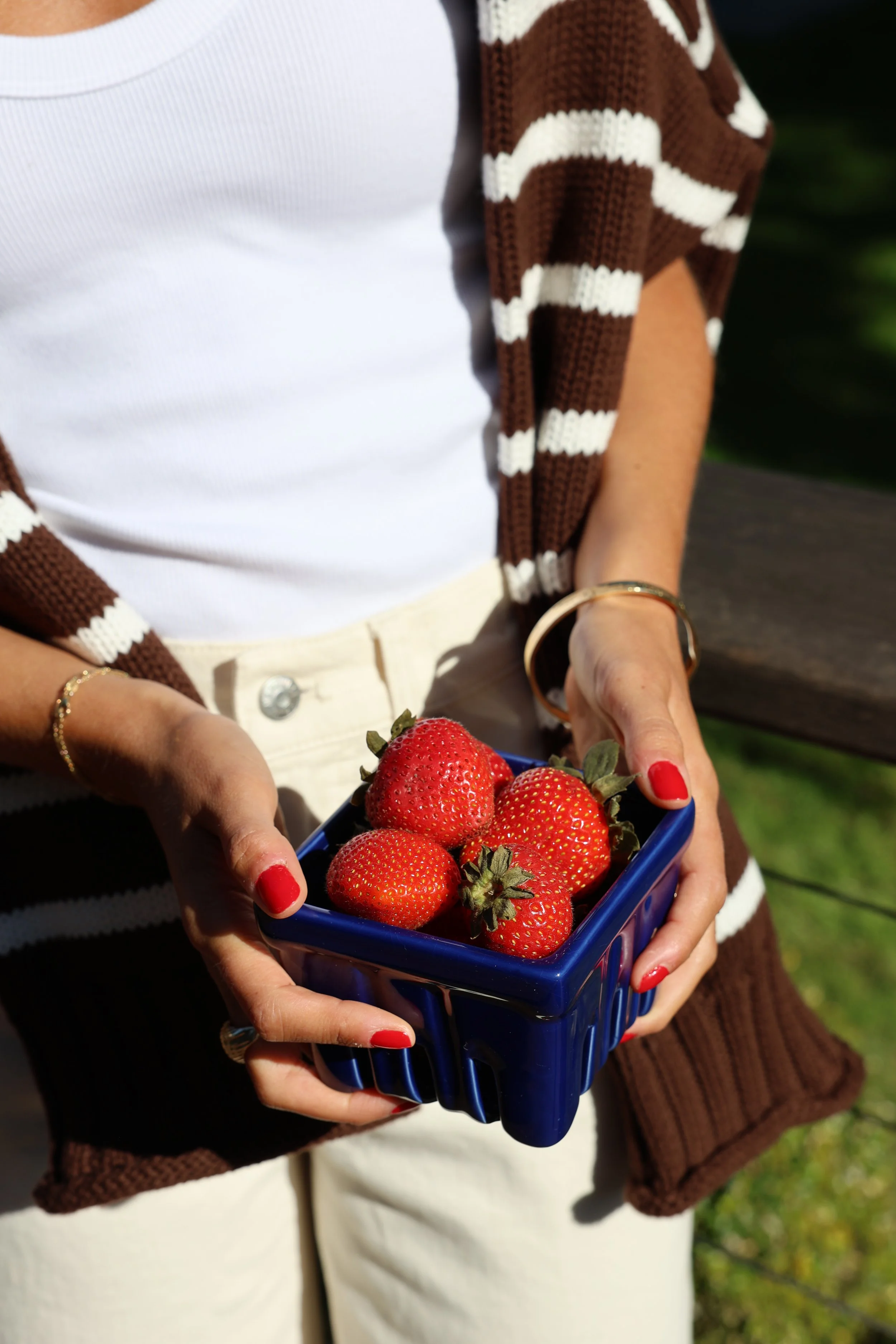 A woman in a white cardigan slicing a lemon on a wooden cutting board in a bright kitchen with a bowl of lemons, a glass of water, and white cabinets in the background.