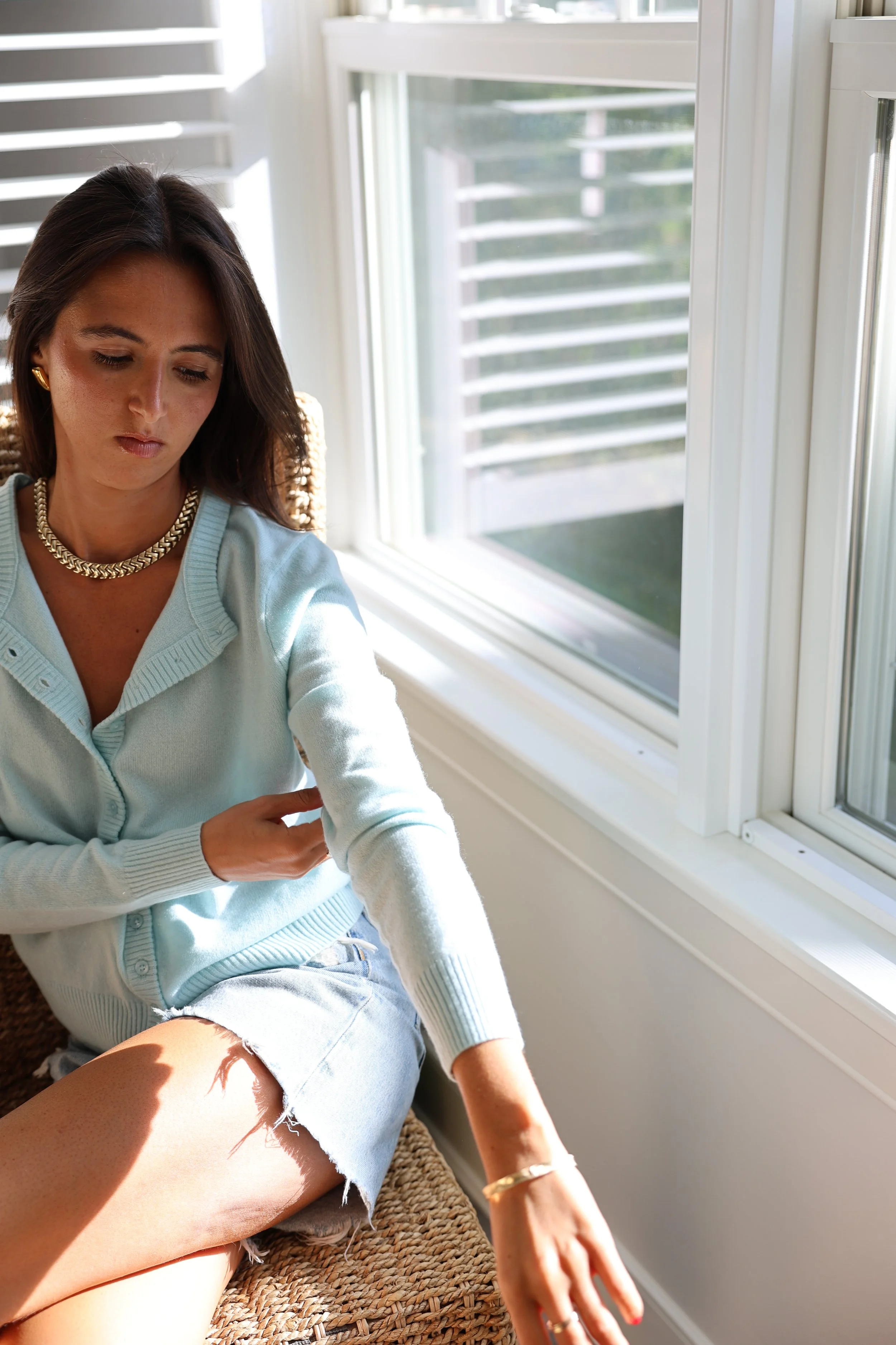 A woman wearing a black long-sleeve crop top and black leggings, outdoors with a wooden fence in the background, pointing with her right hand.