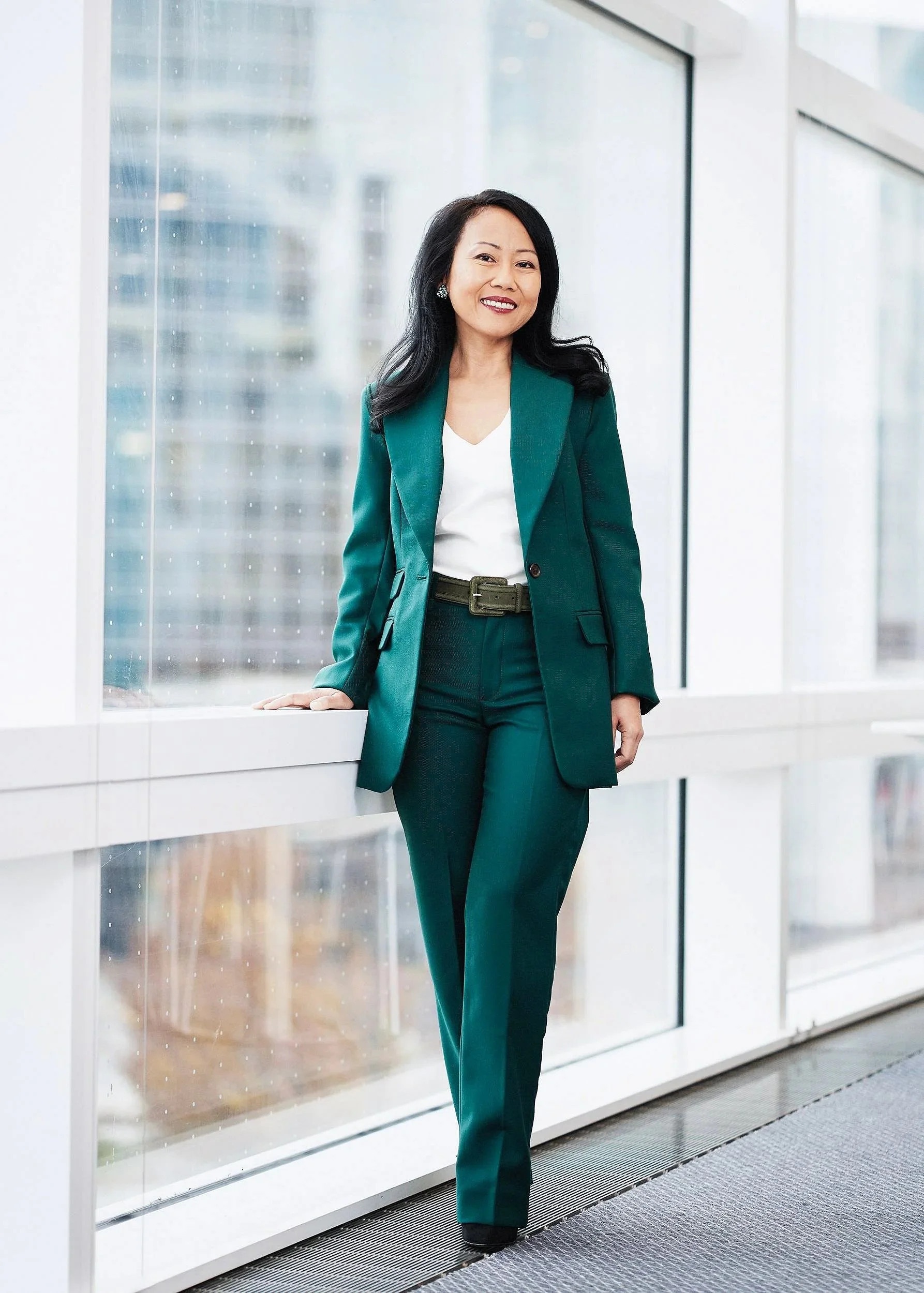 Full-length corporate executive portrait of female business leader in green suit standing in modern office with natural window light.