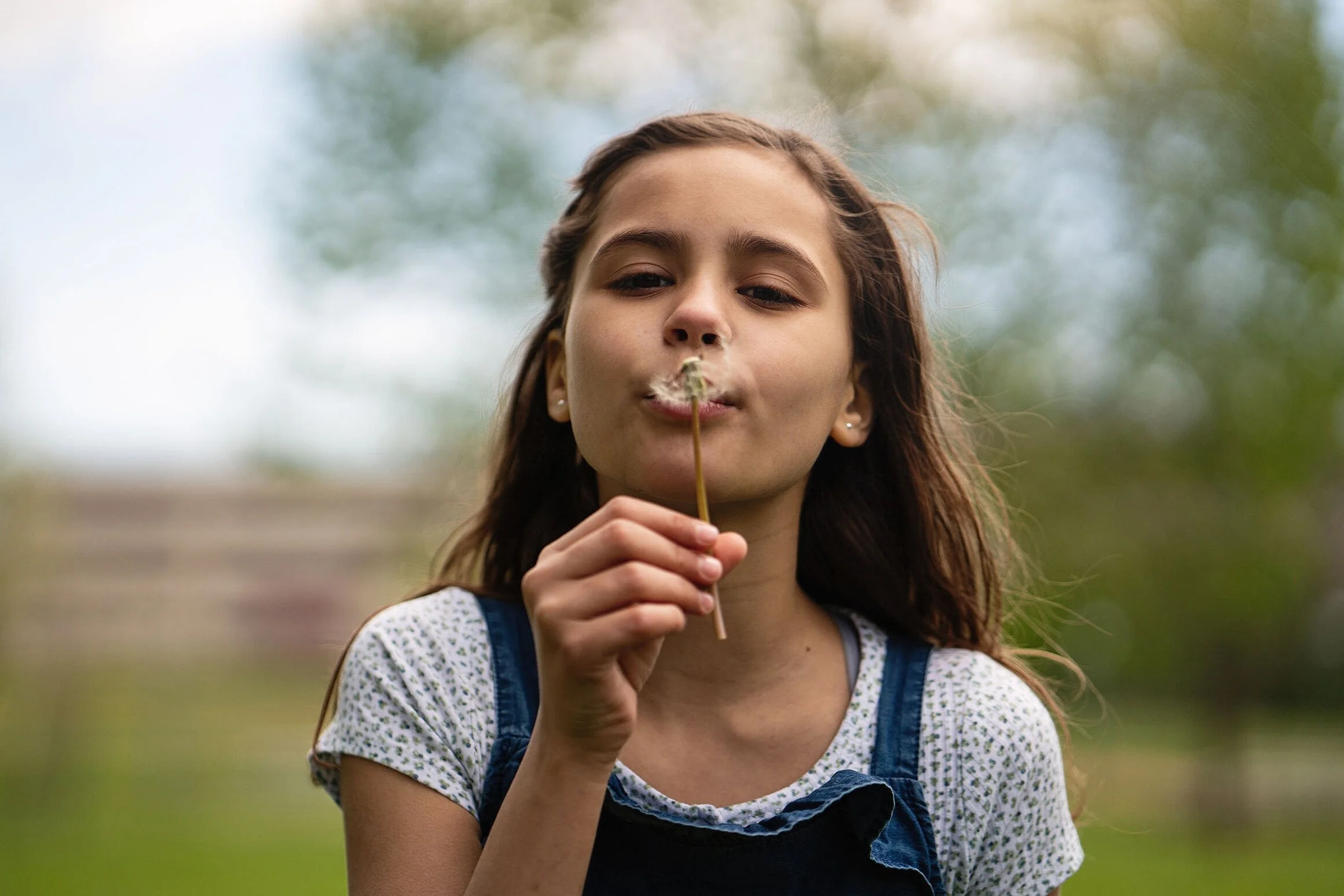 Young girl outdoors blowing on a dandelion