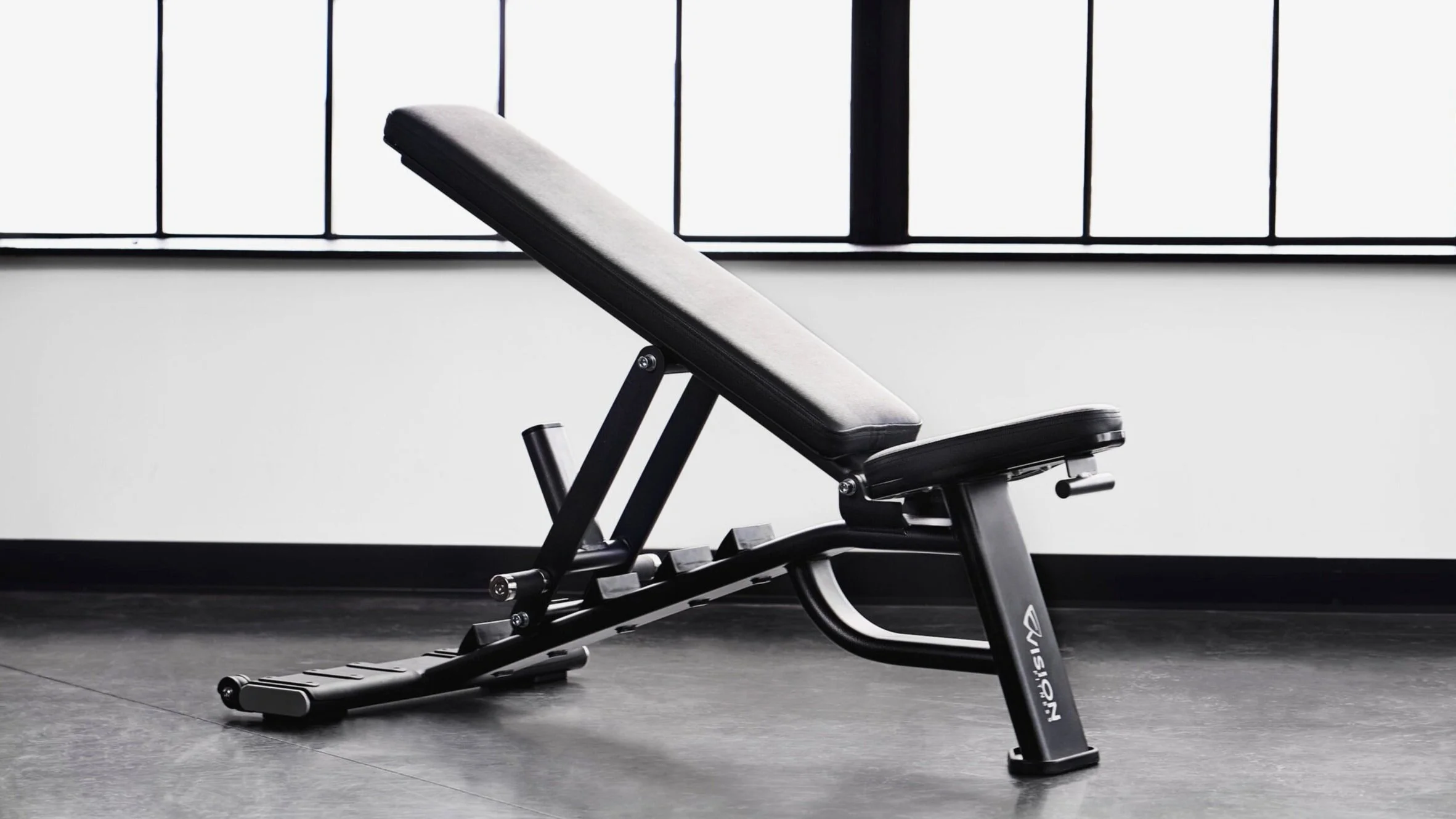 Black adjustable workout bench inside a gym with large windows.
