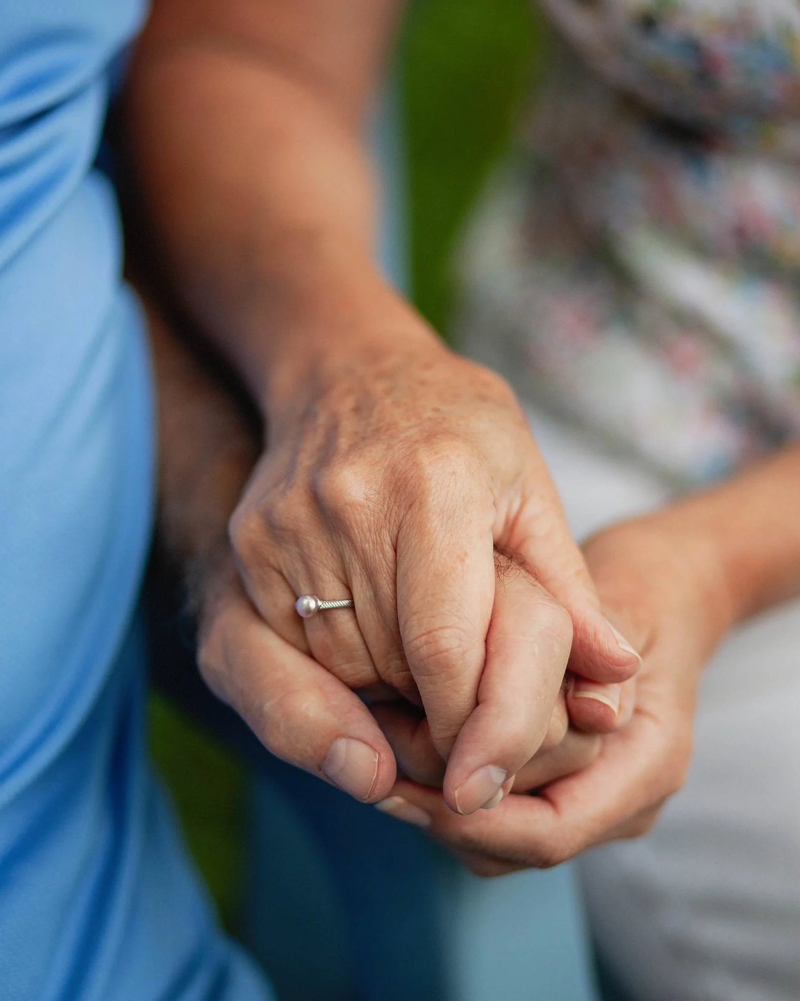 Close-up of two people holding hands, one with a pearl ring, outdoors.
