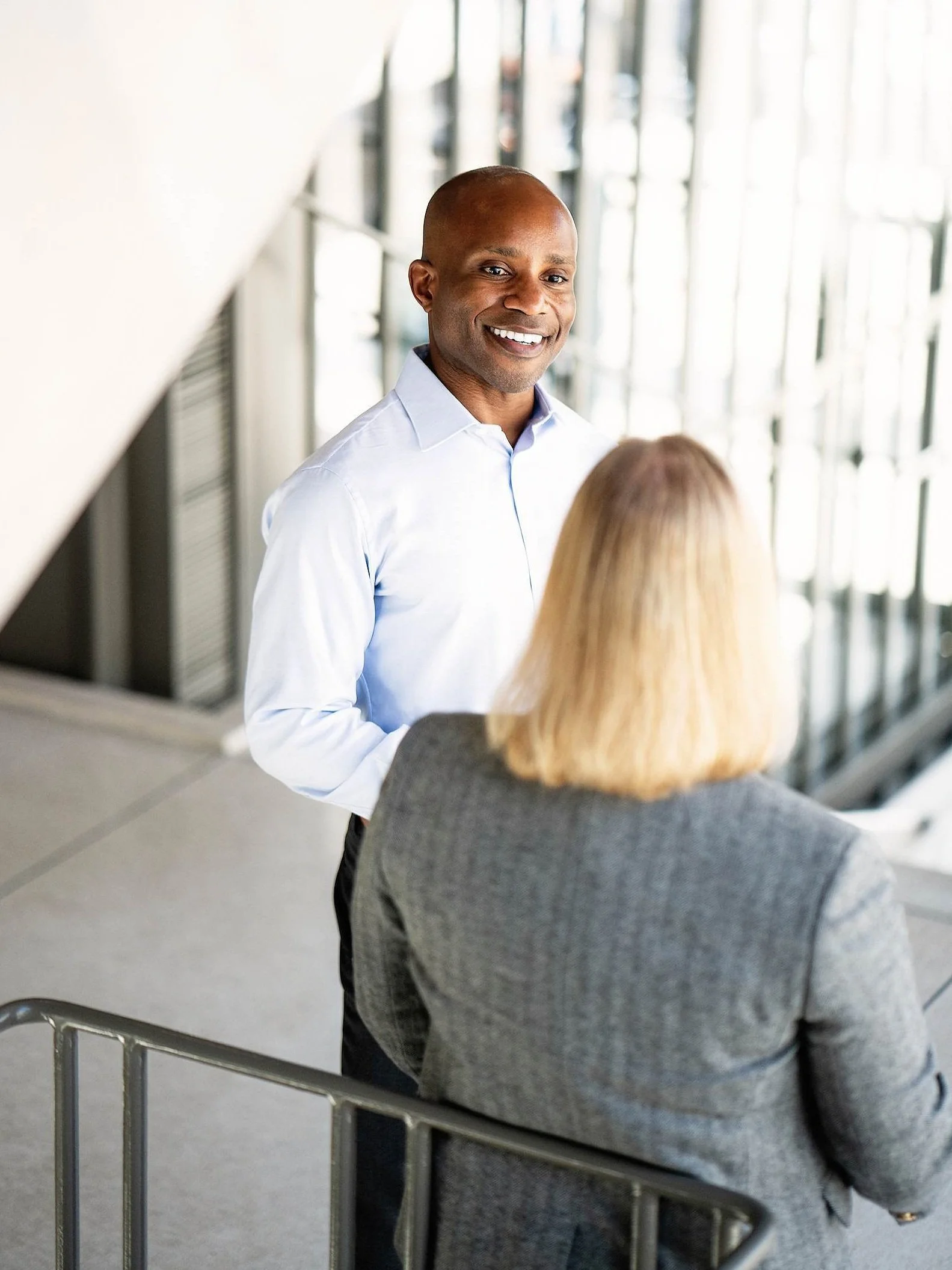 Corporate executive speaking with colleague in modern office stairwell.