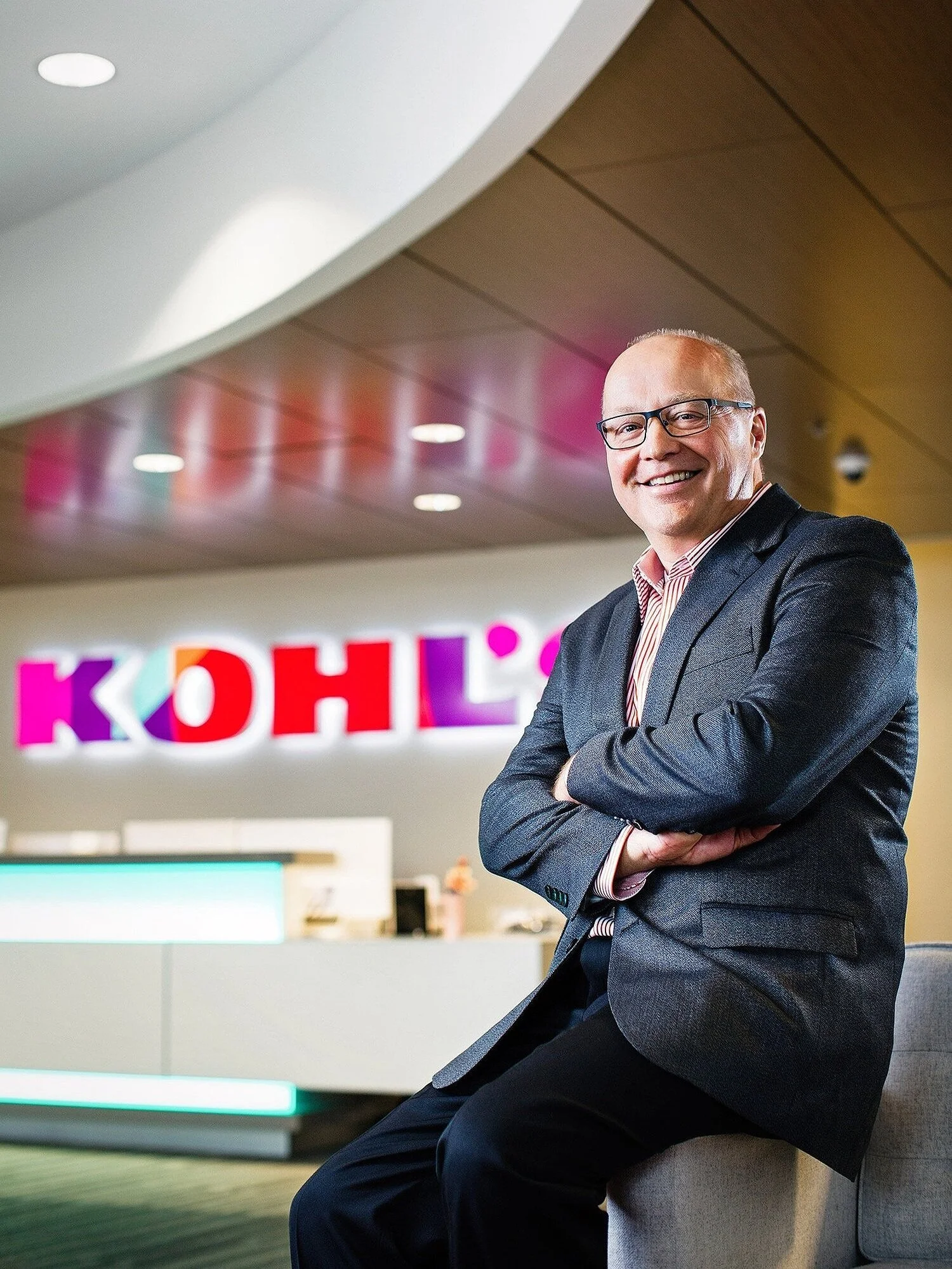 Corporate executive seated in a modern office lobby with illuminated brand signage in the background.