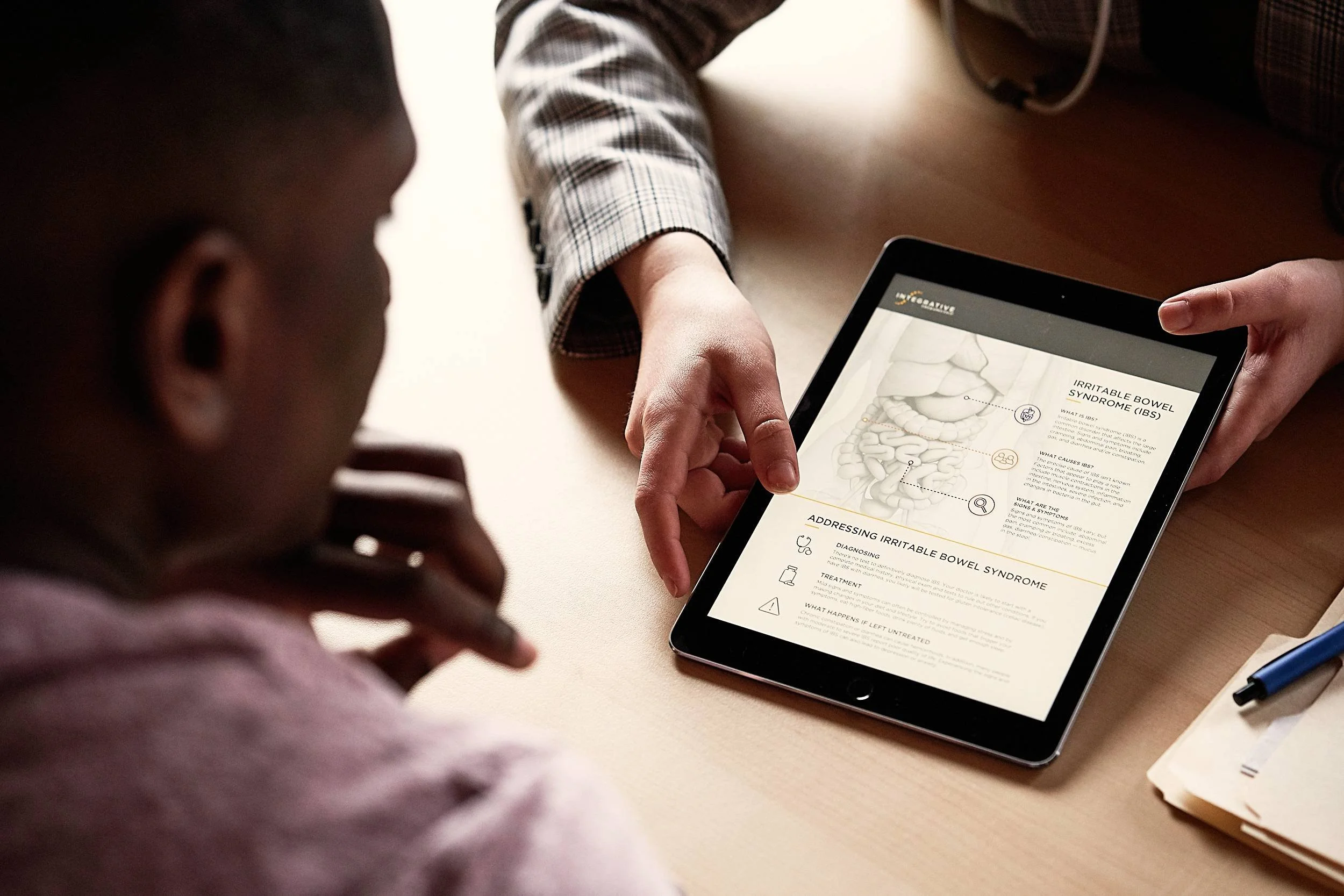 Healthcare provider points to a tablet displaying patient education content about irritable bowel syndrome as a patient looks on.