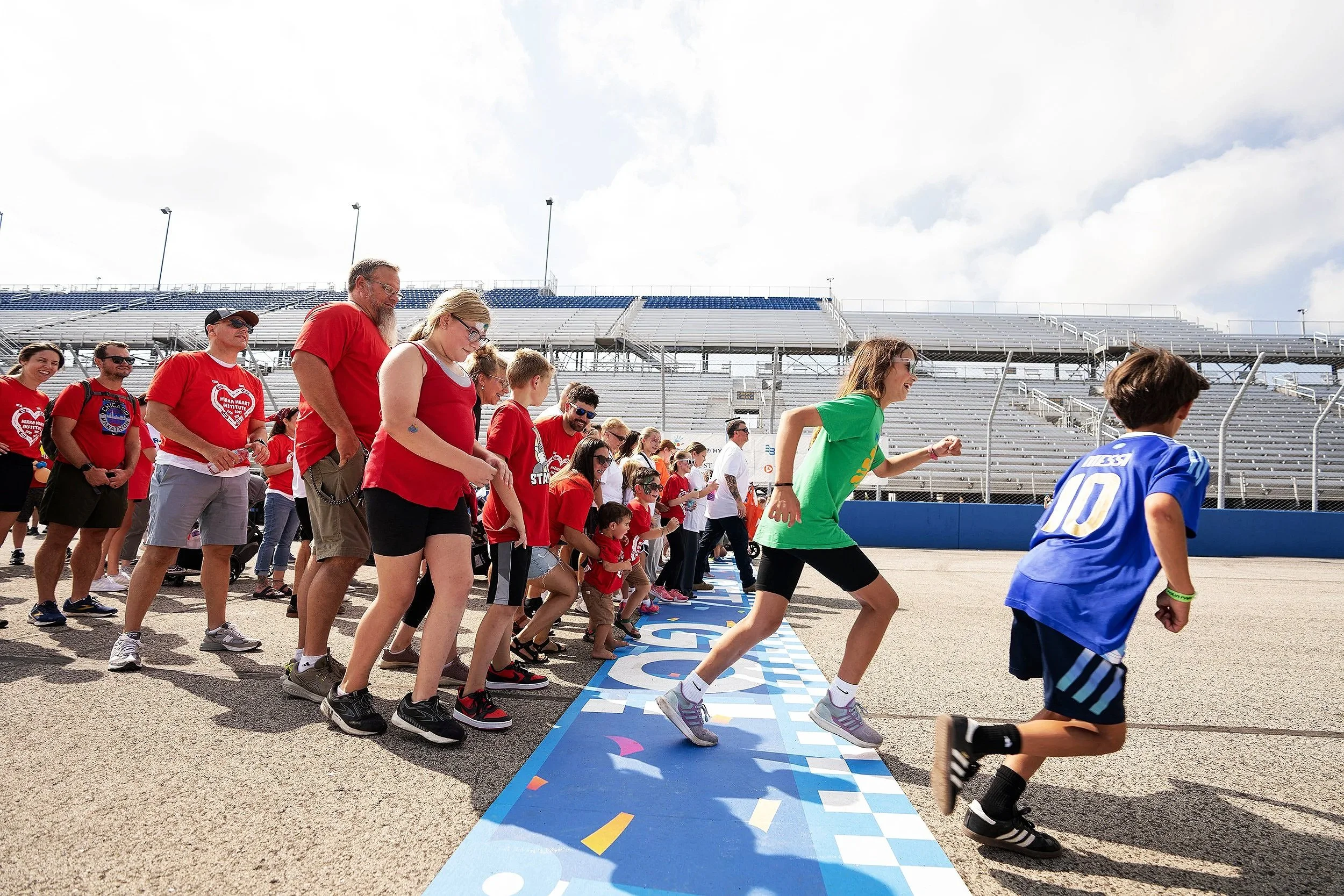 Children and families participate in the Rally Round event at a racetrack, running across the starting line to support Children’s Wisconsin Foundation.