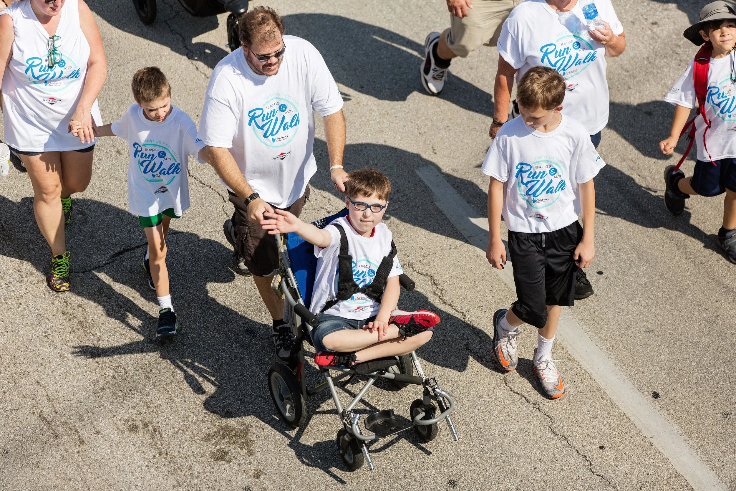 Child using a wheelchair participating in a community charity run with family members.