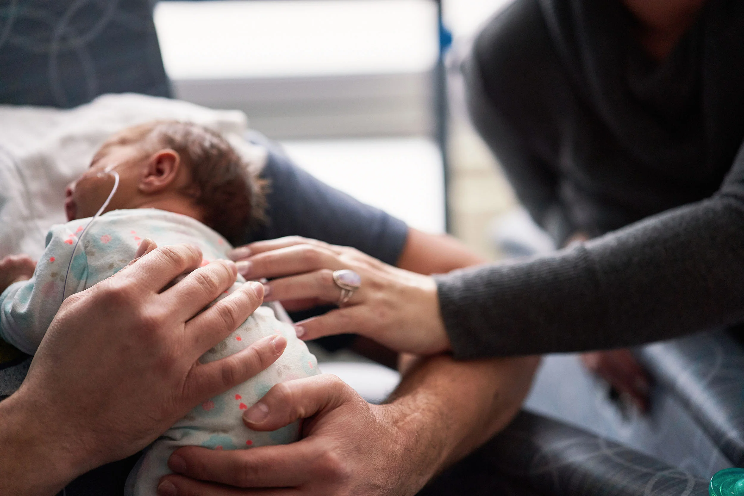 Close-up of a newborn baby in a hospital bed, with a woman and a man comforting and holding the baby.