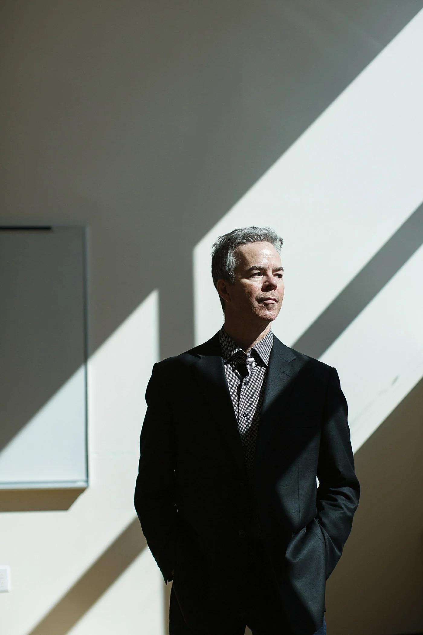 Executive portrait of violinist Frank Almond in black suit standing in modern architectural interior with dramatic natural light.