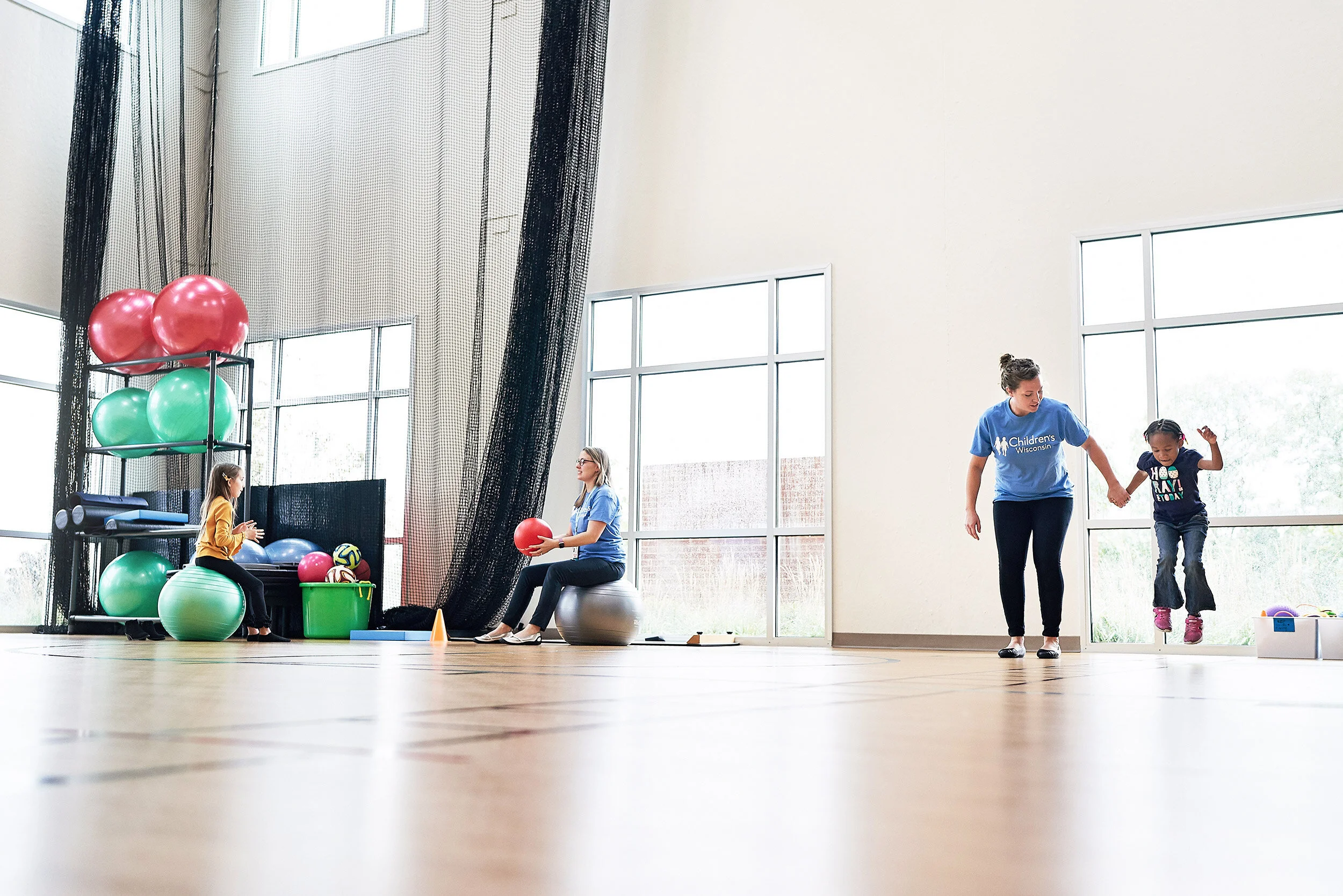 Children and instructor in an indoor gymnasium participating in physical activities with exercise balls and other equipment.
