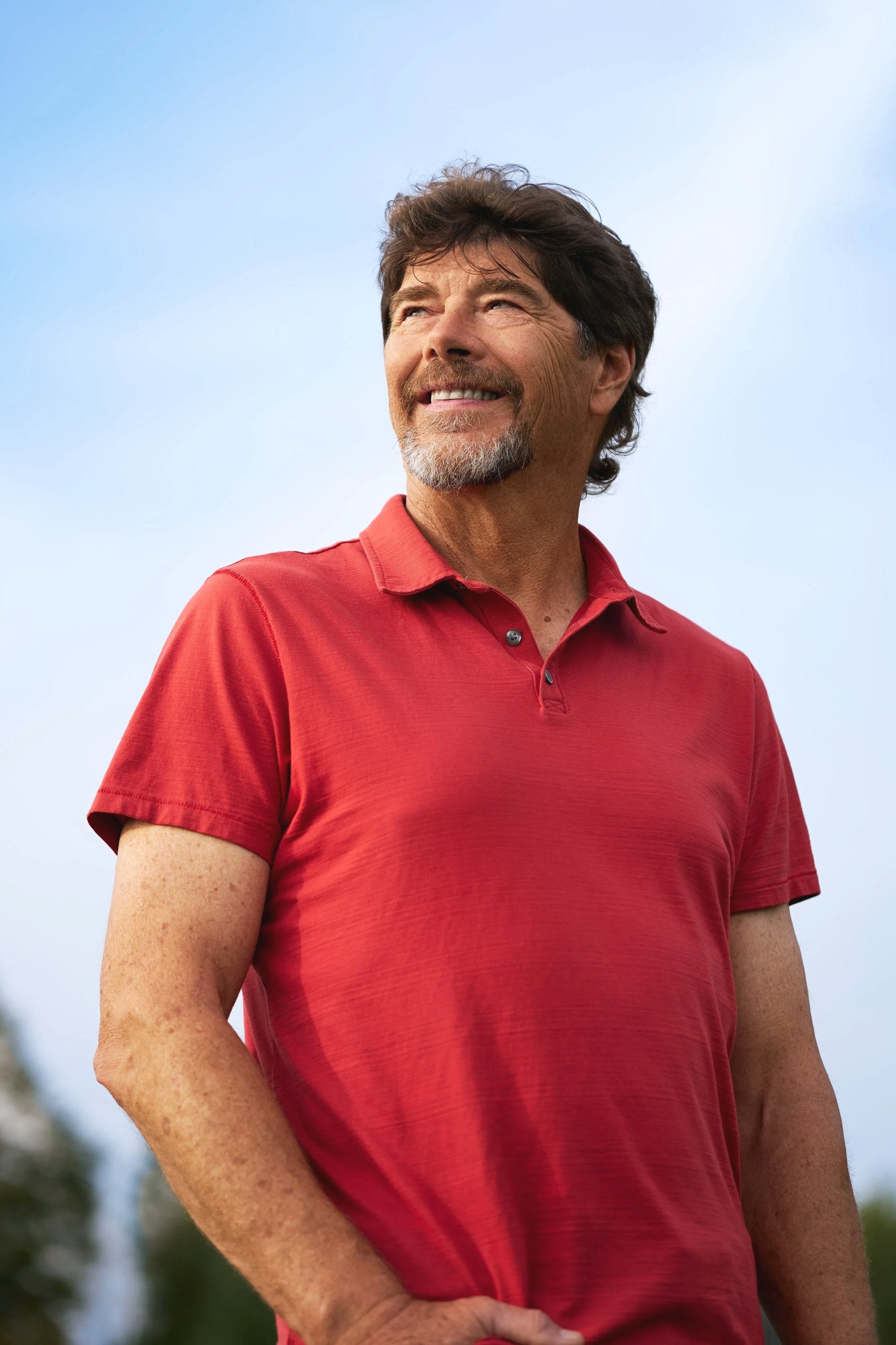 Cancer survivor Jon Stahlecker stands outdoors in a red polo shirt, looking up toward the sky, photographed for Mayo Clinic Maga