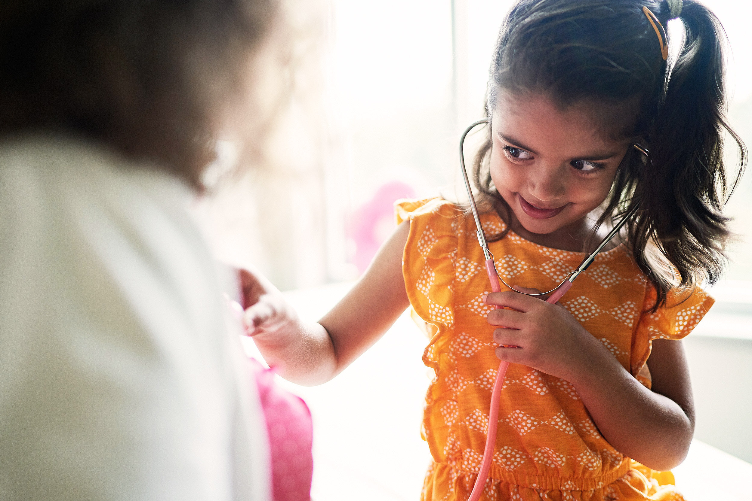 A young girl with a stethoscope listening to another child's chest during a play doctor activity.