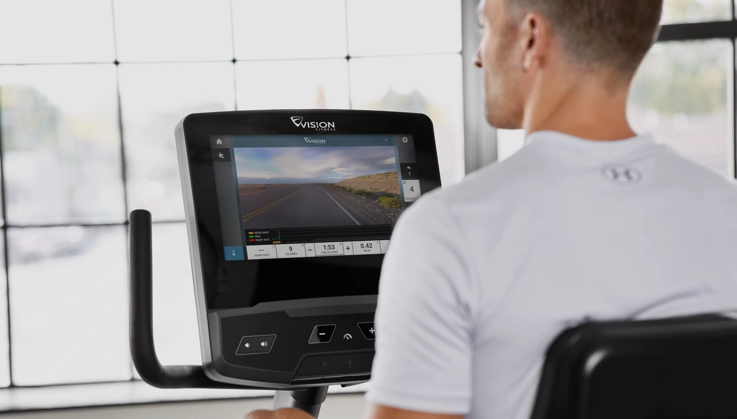 A person with short hair using a fitness machine with a screen displaying a virtual outdoor road scene.