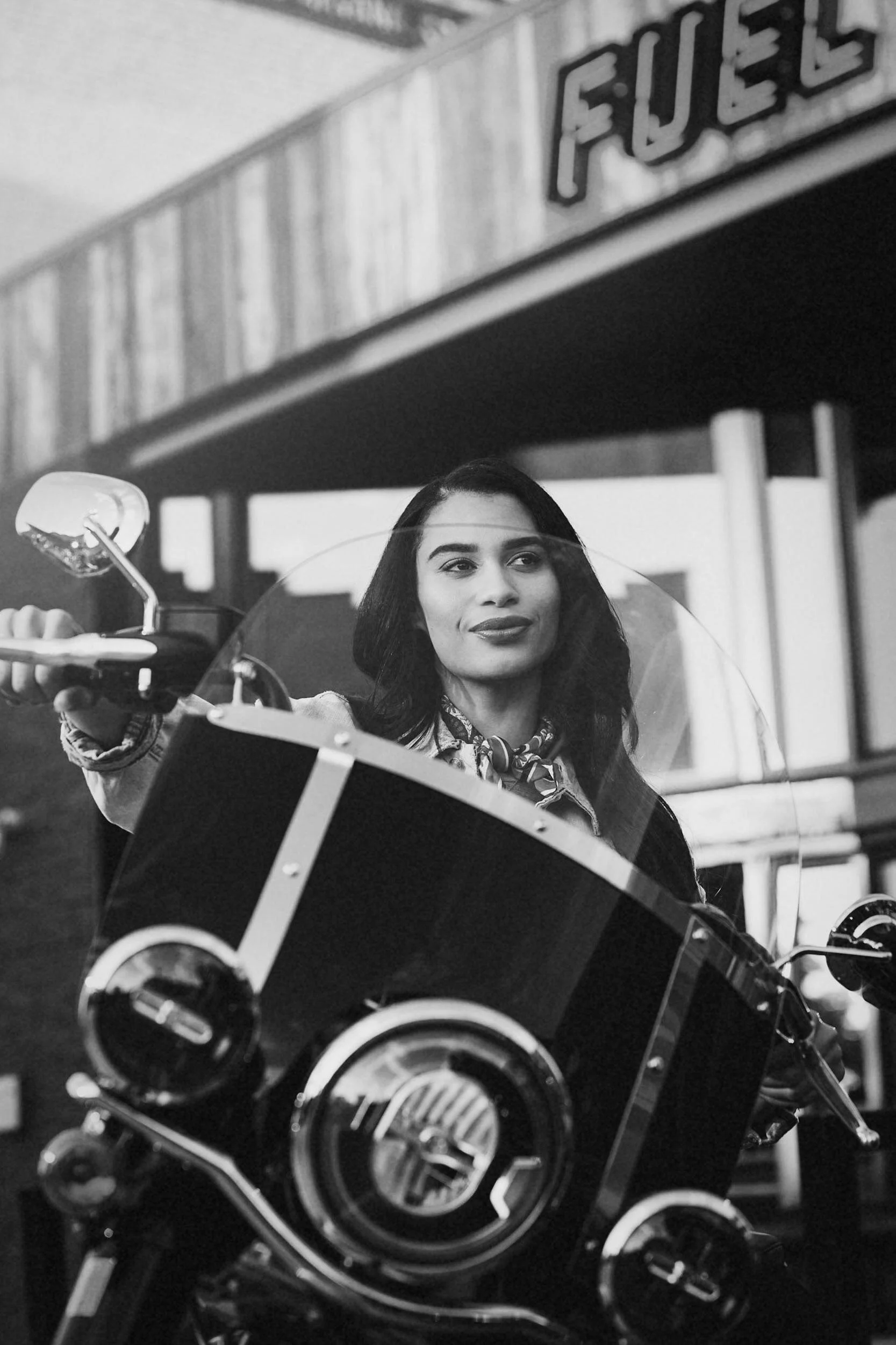 A woman sitting on a motorcycle in front of a vintage store with a sign that reads "FUEGO"