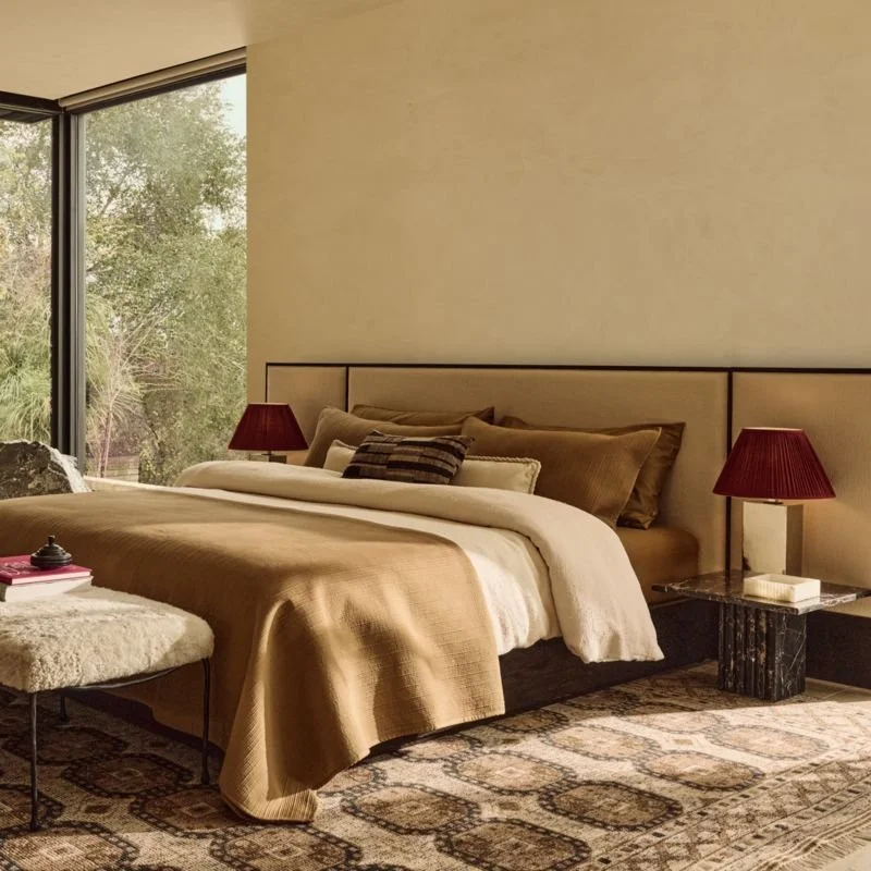 Habitación elegante con cama grande, almohadas, mesitas con lámparas rojas y ventana grande con vista a árboles y naturaleza.