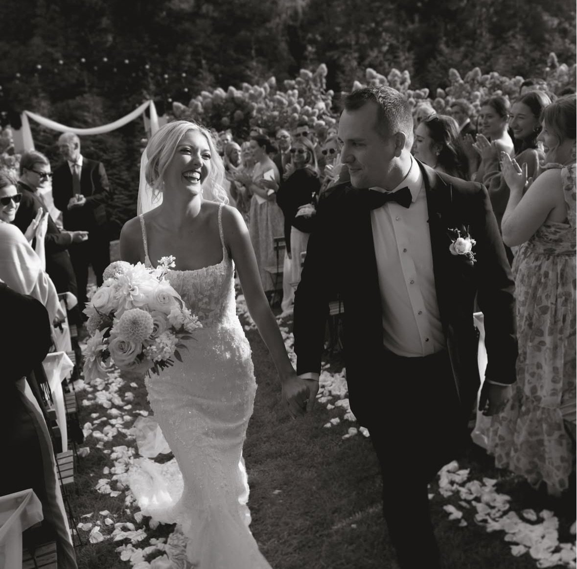Bride and groom walking down aisle, smiling, surrounded by guests.