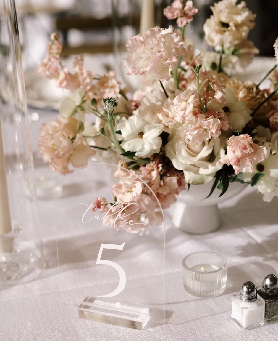 Wedding table centerpiece with pink and white flowers, acrylic table number five, candle, and salt and pepper shakers.