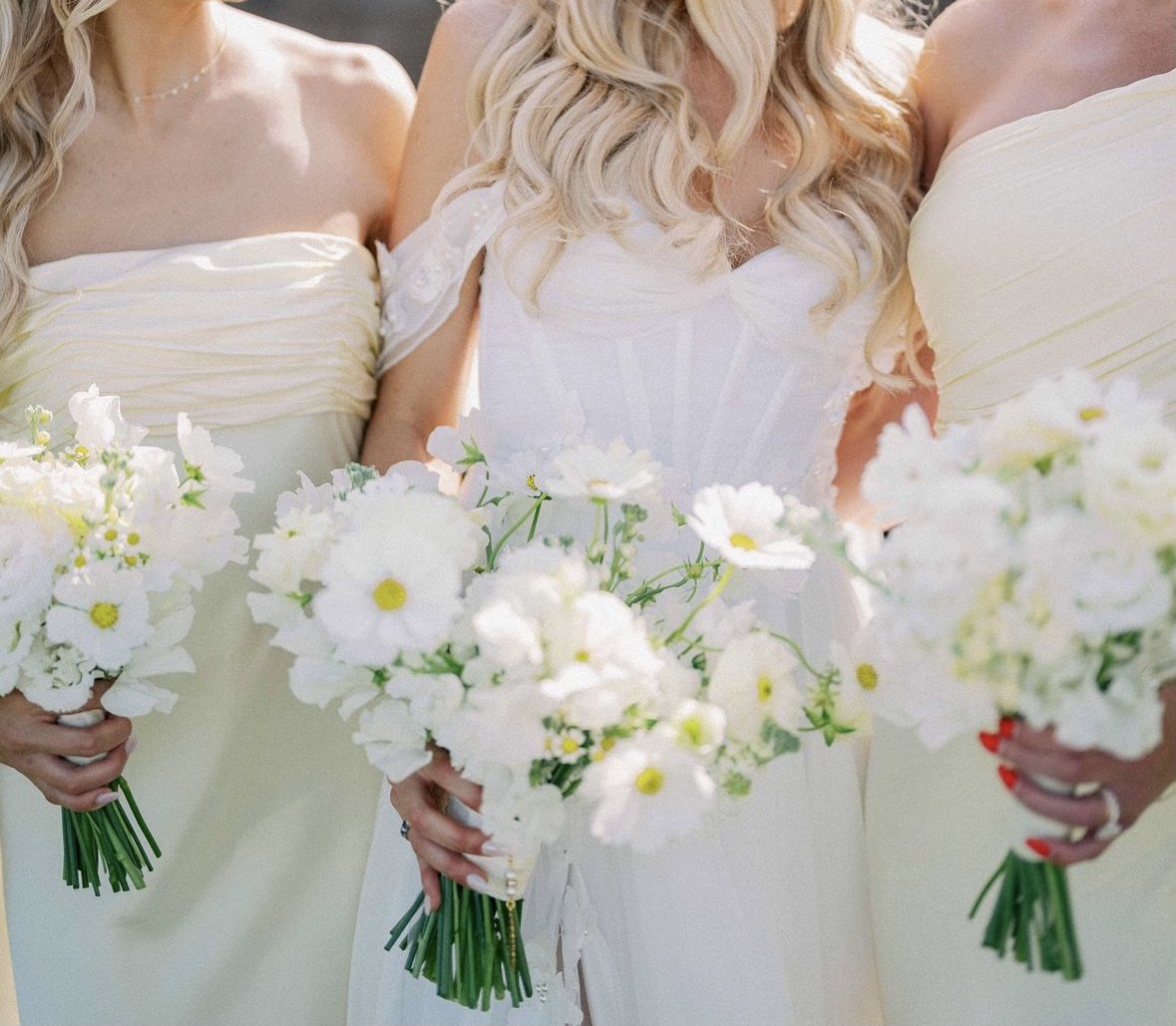 Three women in light-colored strapless dresses holding bouquets of white flowers.