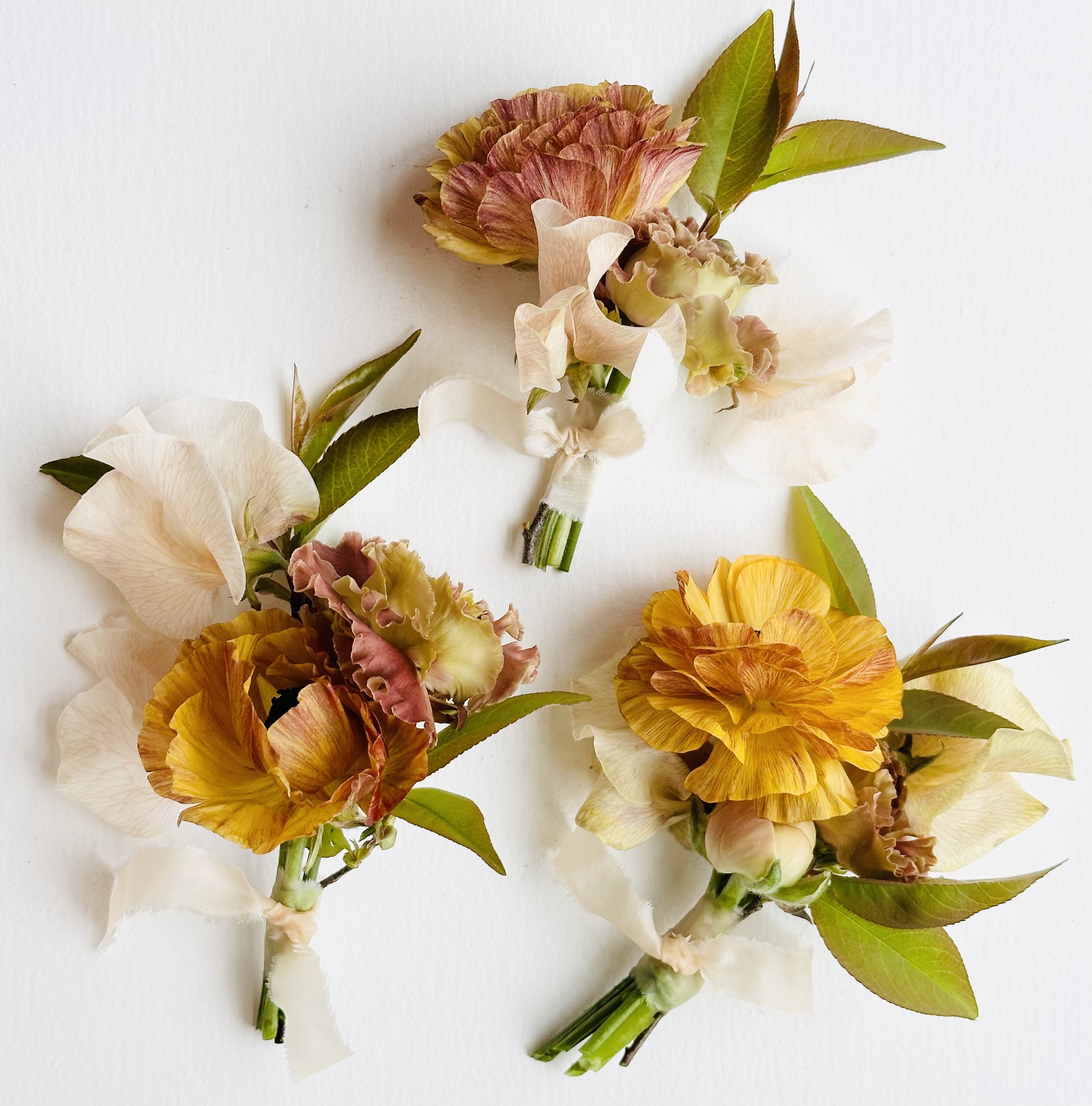 Three small floral arrangements with yellow and pink flowers tied with ribbon and green leaves on a white background.