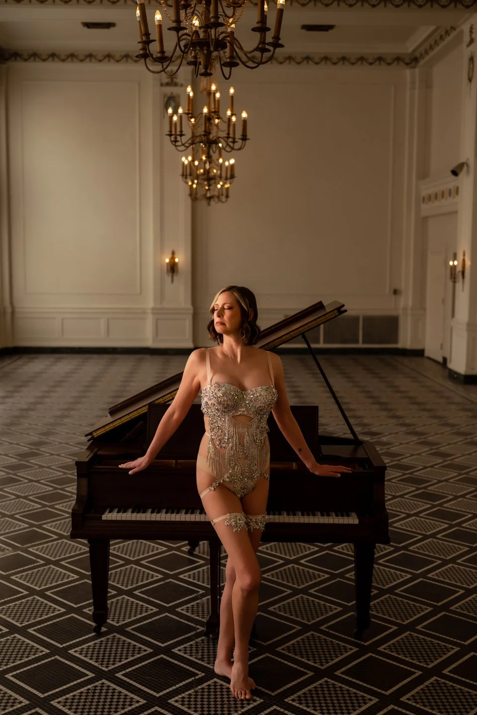 Woman in showgirl outfit in front of a piano in a ballroom. 