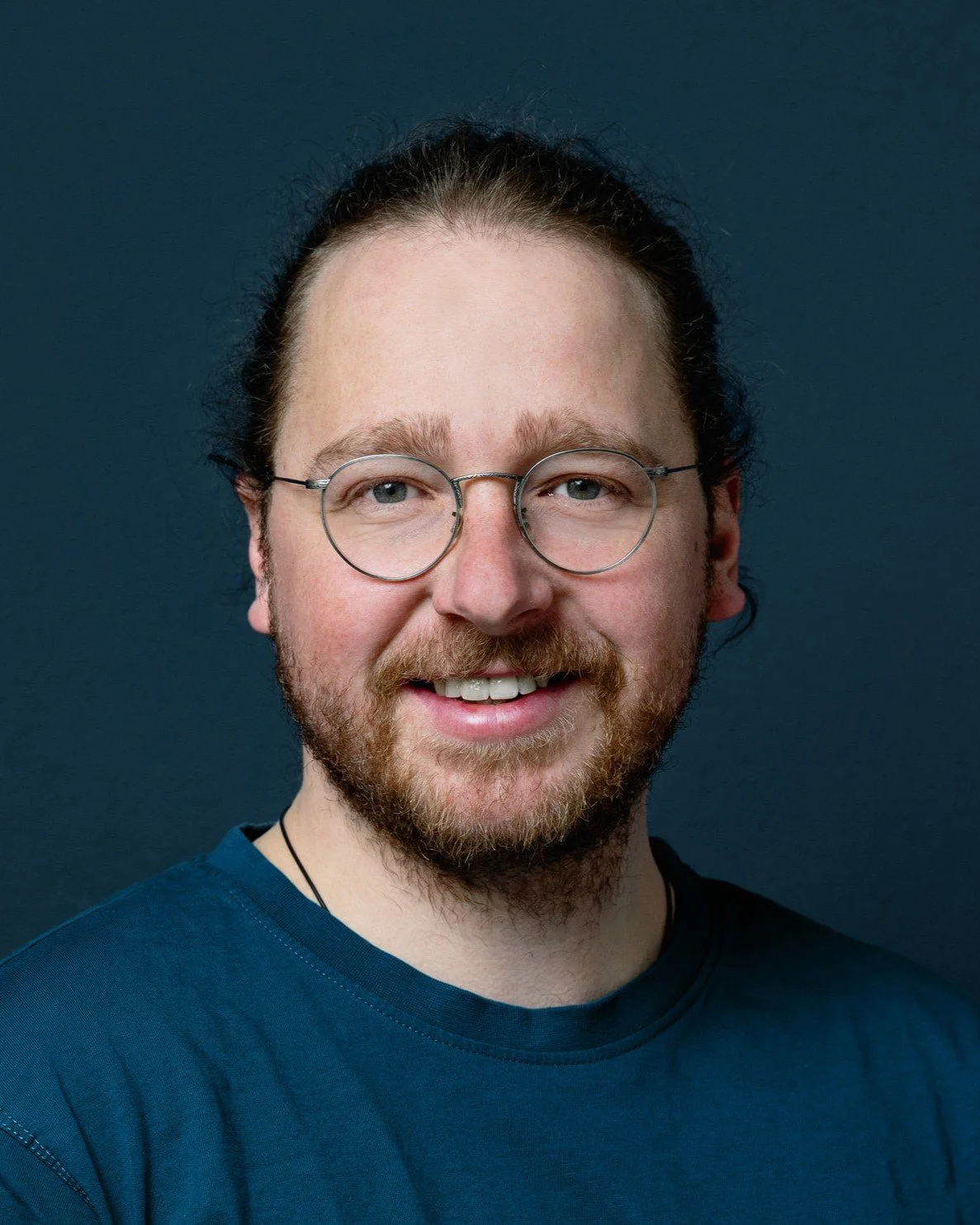 Portrait eines lächelnden Mannes mit Bart und Brille vor einem dunklen Hintergrund