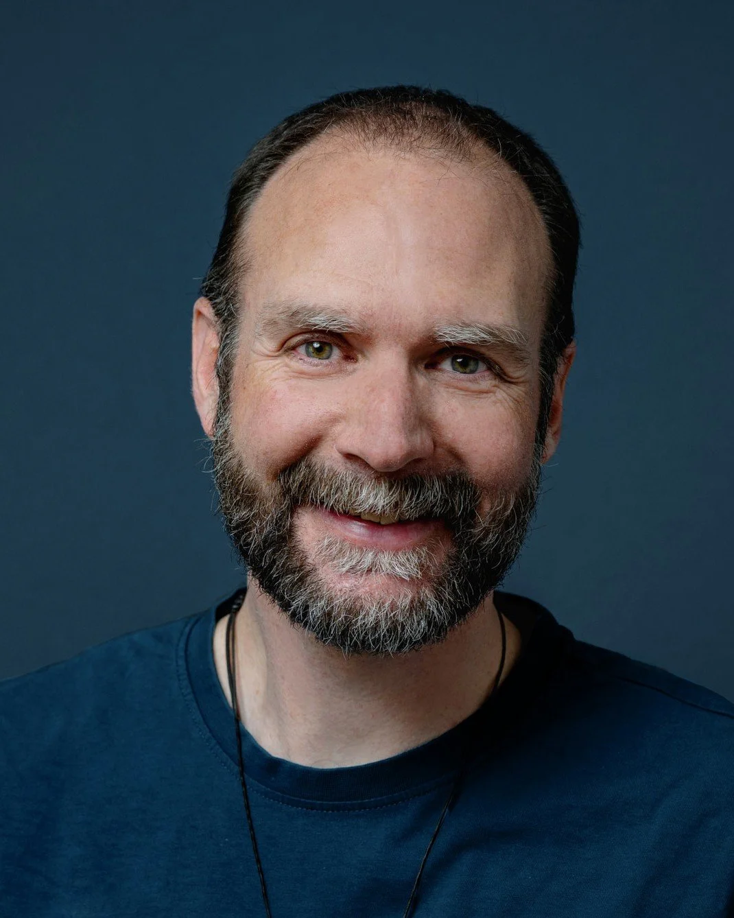 Portrait eines lächelnden Mannes mit Bart vor einem dunklen Hintergrund