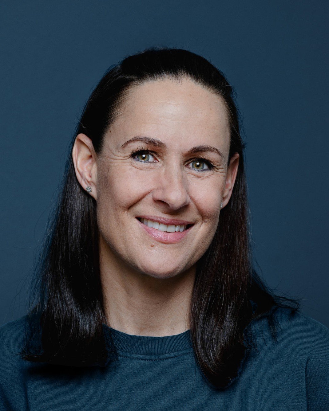 Portrait einer lächelnden Frau mit langen dunklen Haaren vor einem blauen Hintergrund
