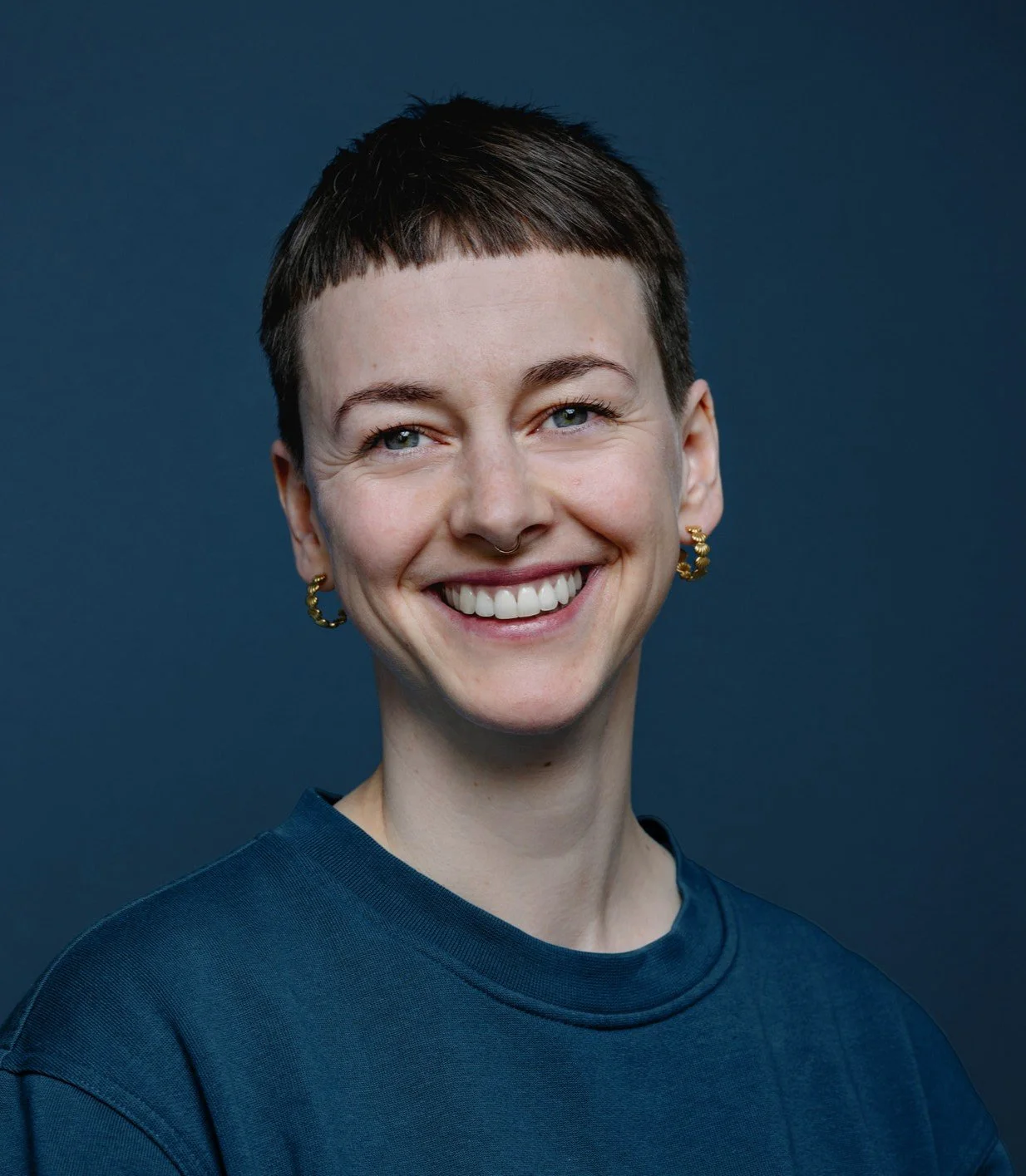 Portrait einer lächelnden Frau mit kurzen braunen Haaren vor einem dunklen Hintergrund