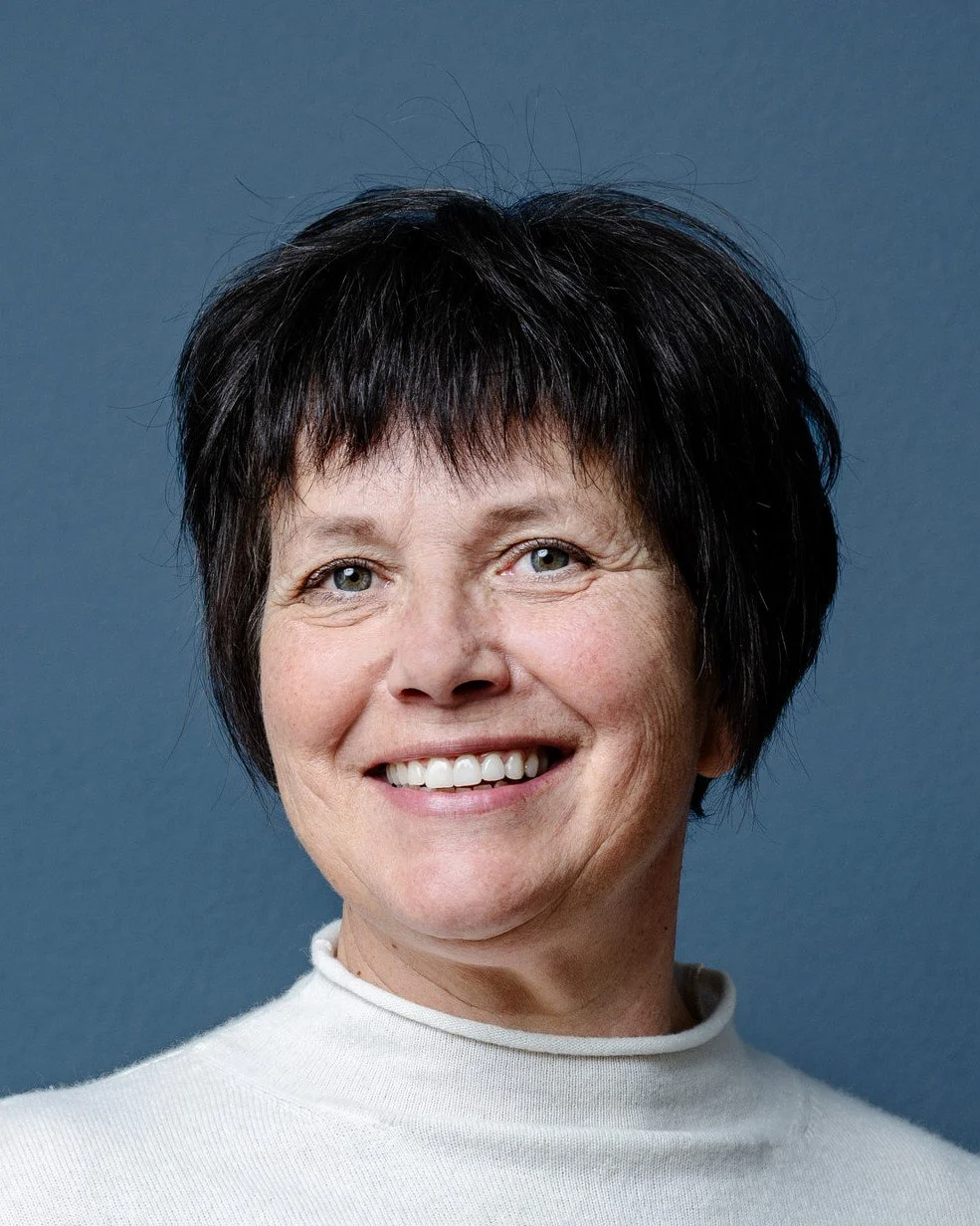 Portrait einer lächelnden Frau mit schwarzen kurzen Haaren vor einem blauen Hintergrund