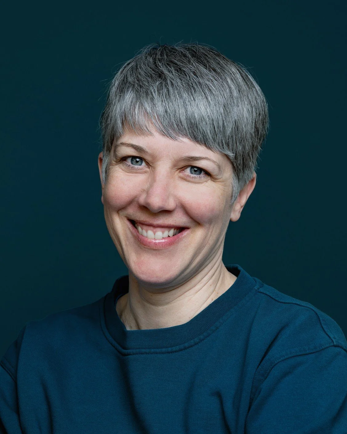 Portrait einer lächelnden Frau mit grauen kurzen Haaren vor einem dunklen Hintergrund